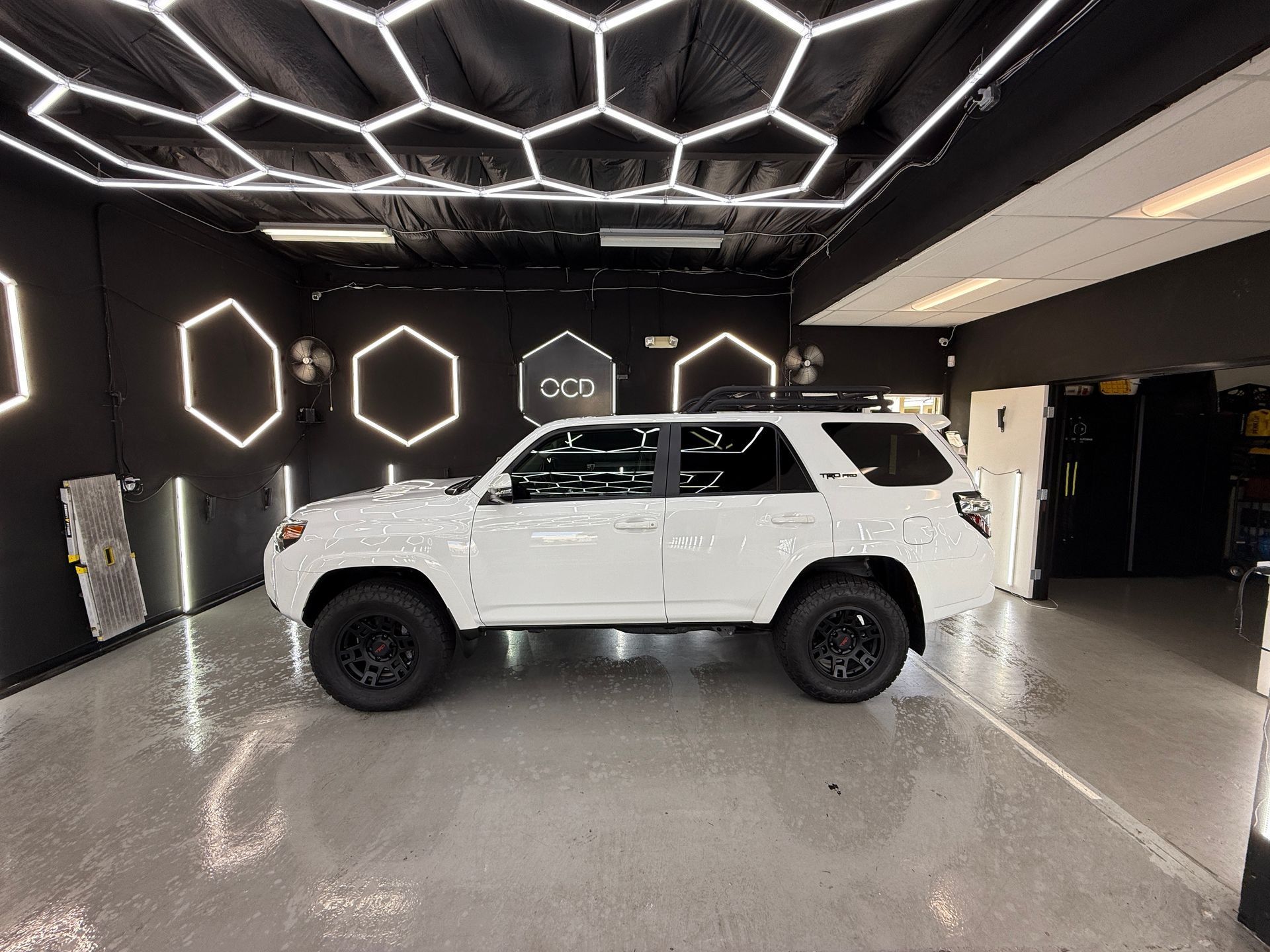 White SUV in a modern showroom with geometric LED ceiling lights and black walls