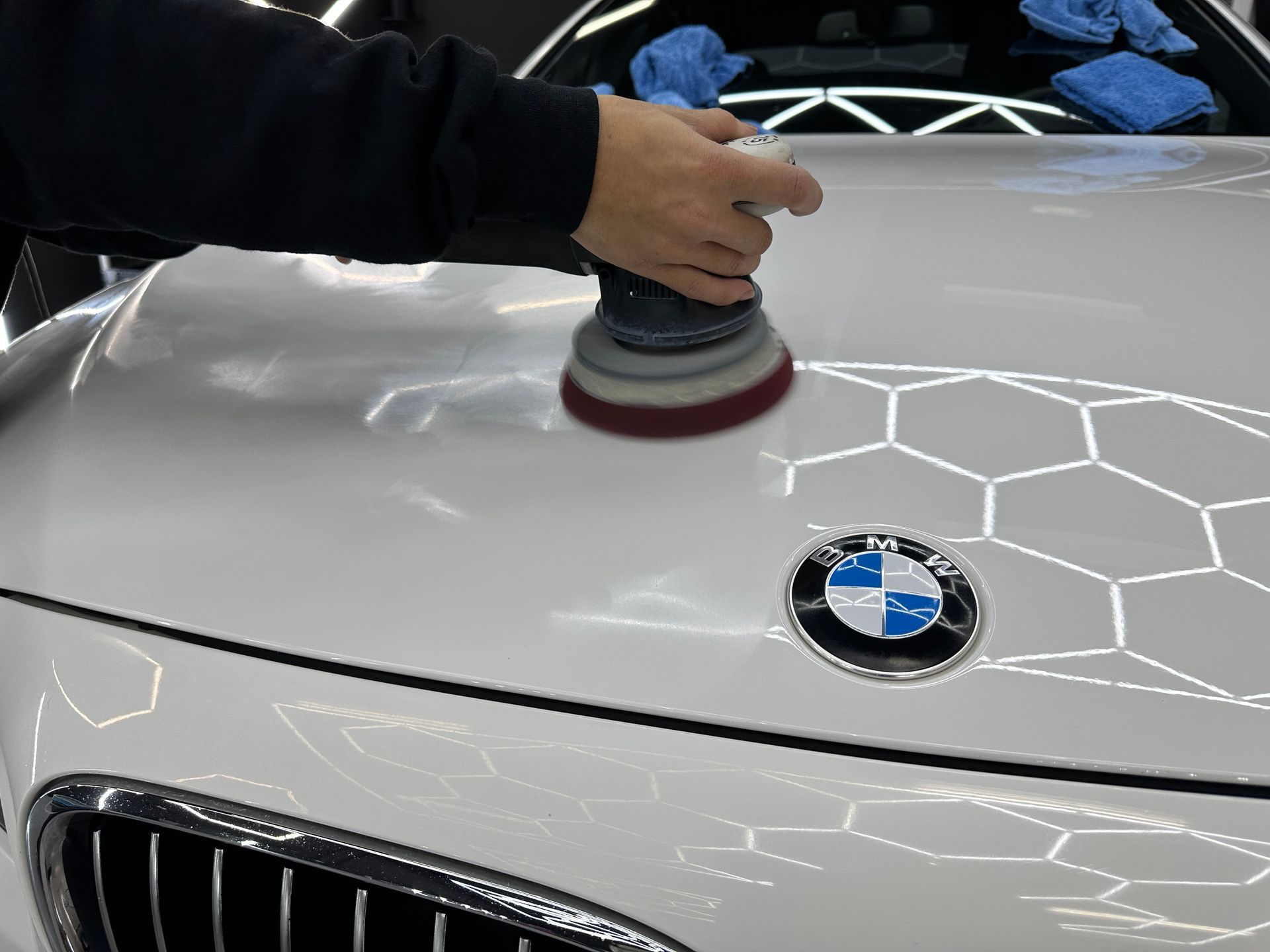 Hand polishing a white BMW hood with a buffer tool, reflections visible on the paint