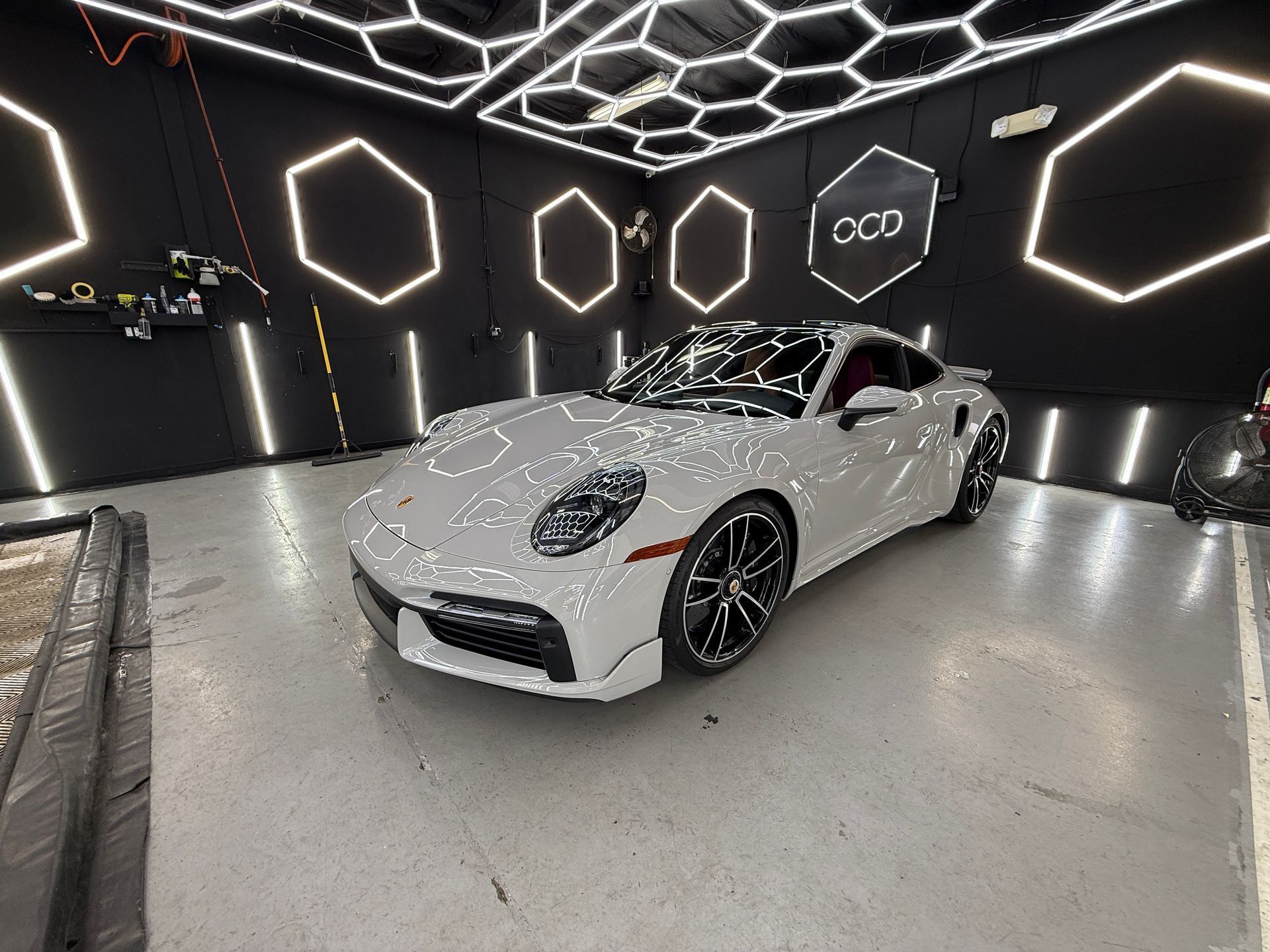 White sports car in a black showroom with glowing hexagonal lights on the walls and ceiling