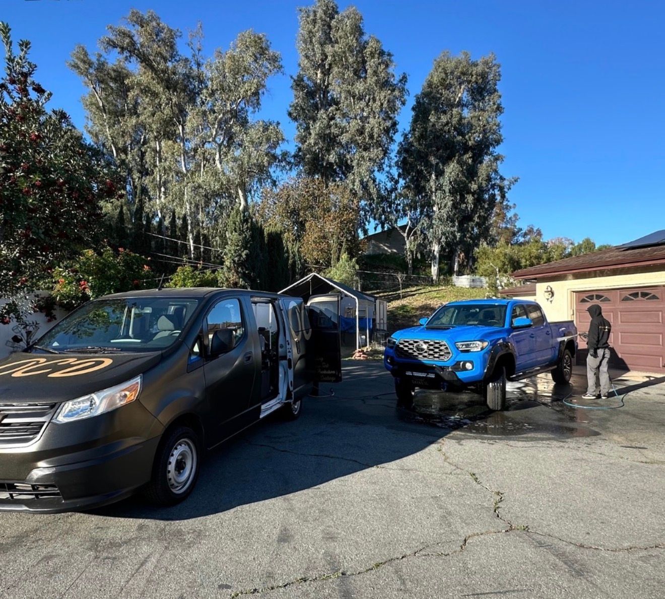 Two parked trucks in a driveway, one black and one blue, with a person standing nearby.