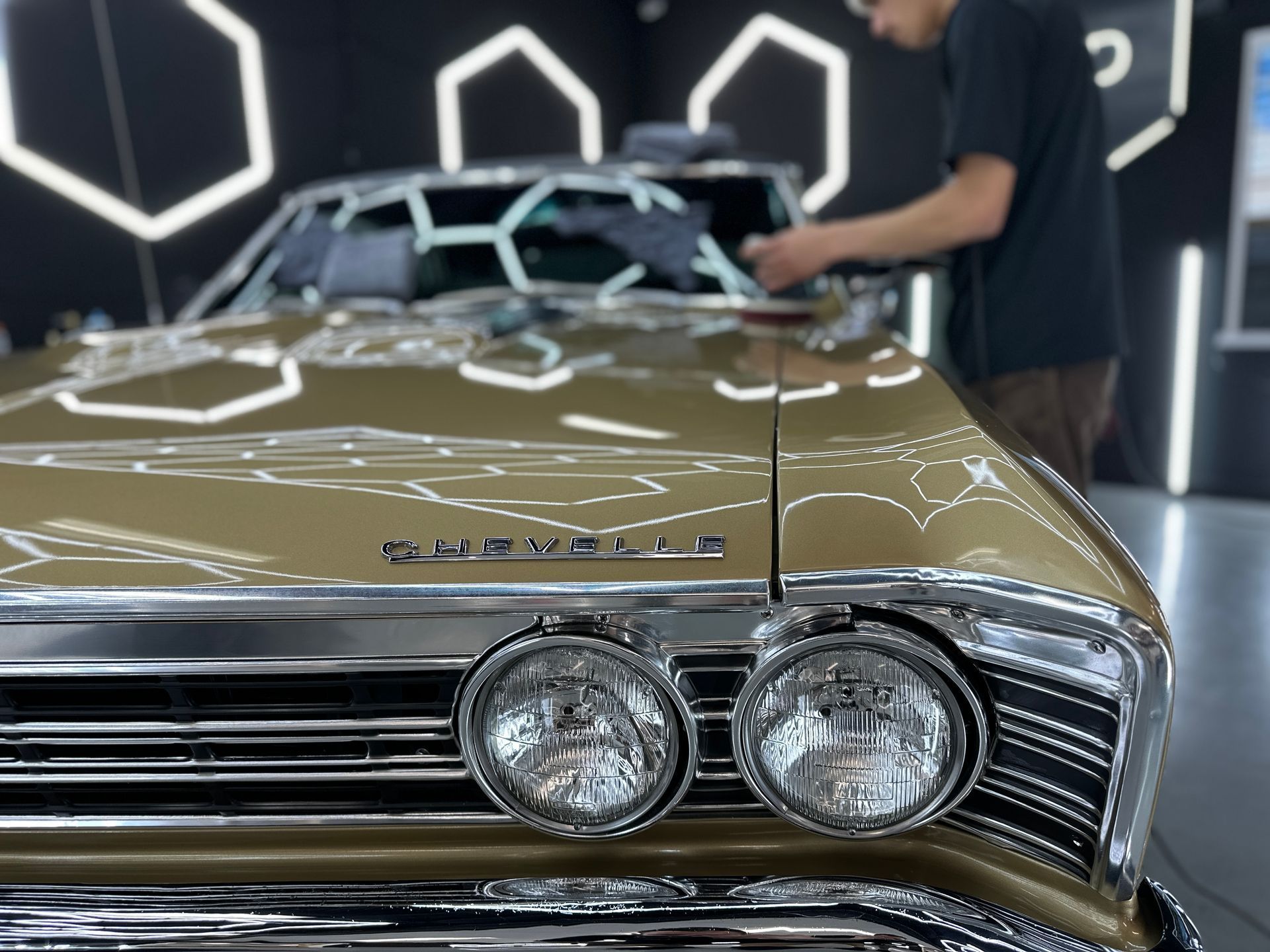 Classic gold convertible under showroom lights, viewed from the front with a person standing beside it