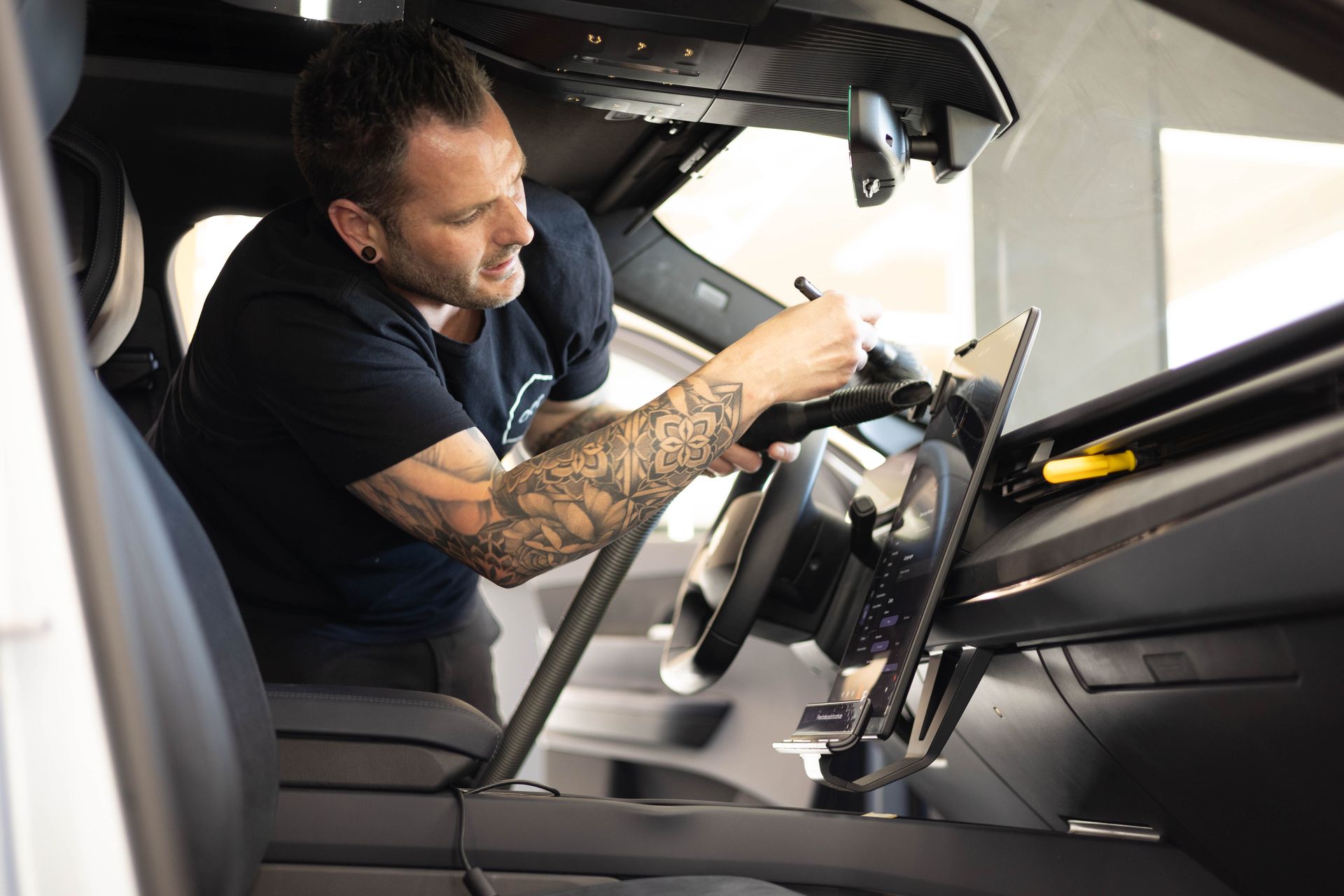 Person crouching beside a black car in a lit auto detailing bay with hexagon lights.