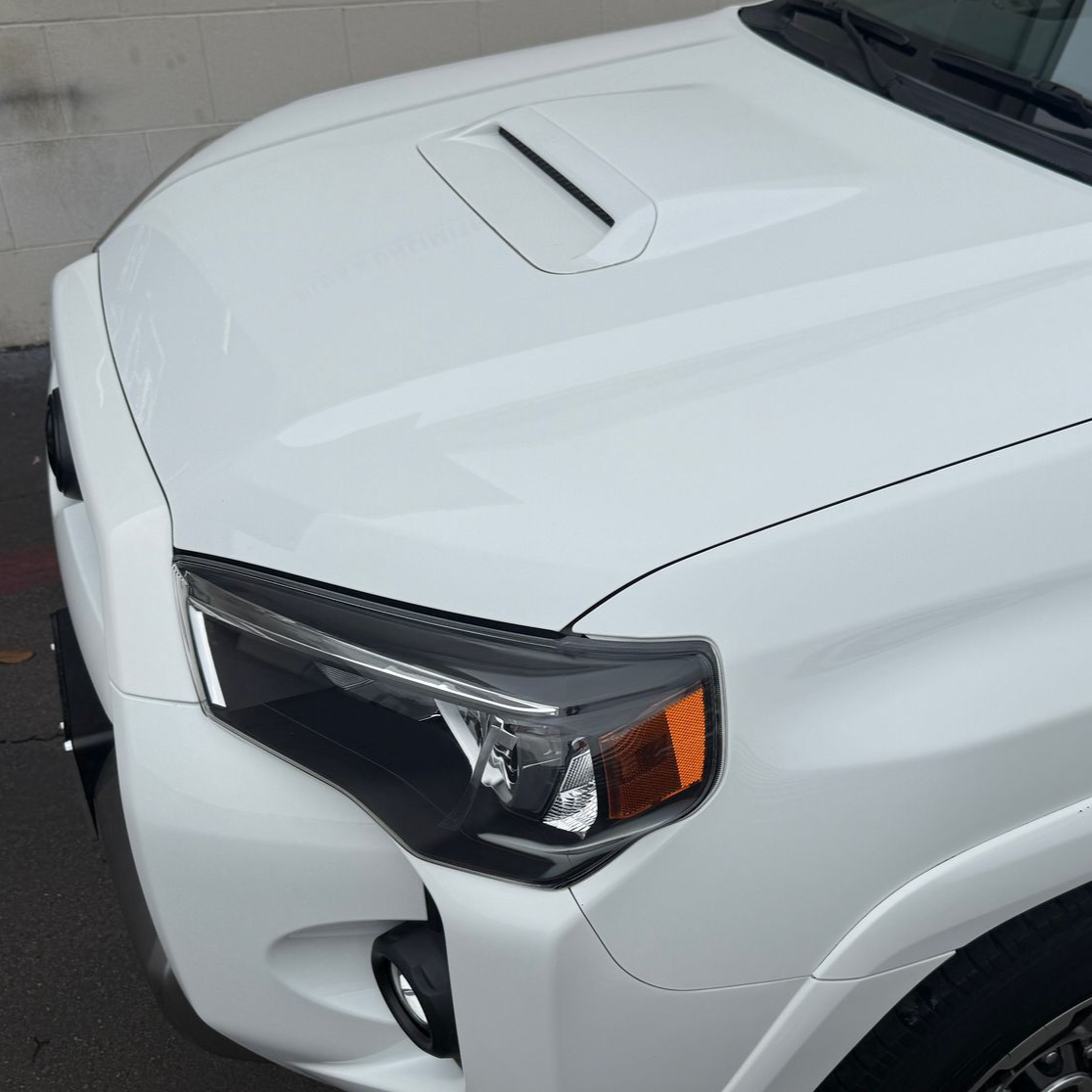 Close-up of a white pickup truck’s front corner, headlight, and hood vent
