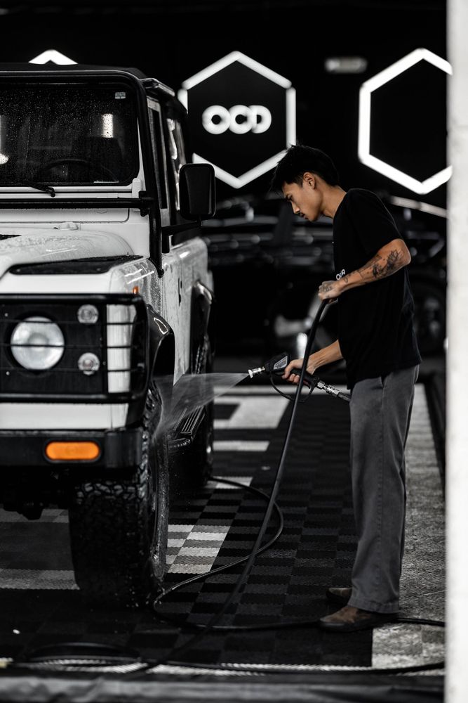 Man washing a white off-road vehicle in a car detailing bay with neon hexagon lights