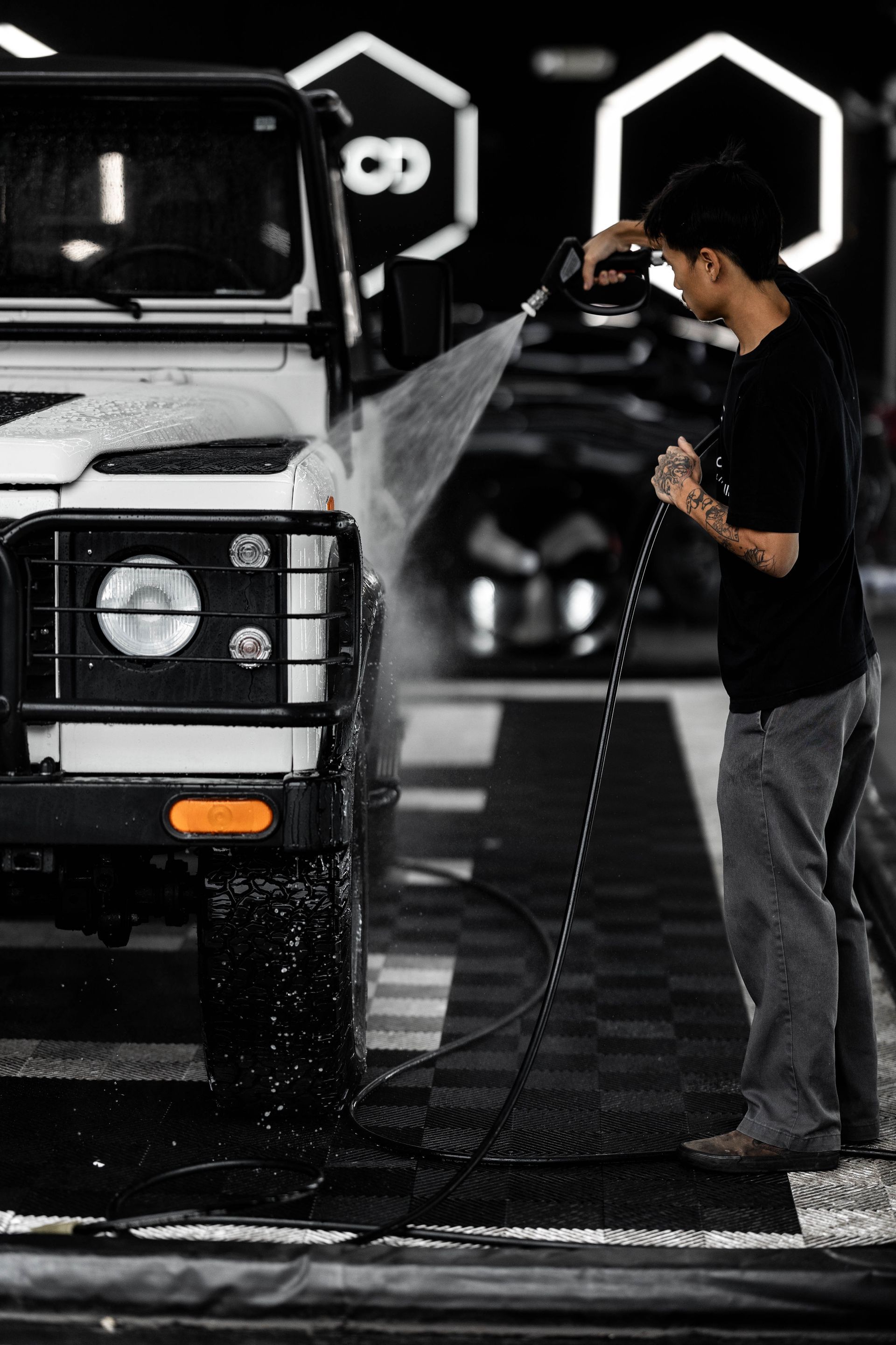 Man washing a white off-road vehicle at a car wash with a pressure hose