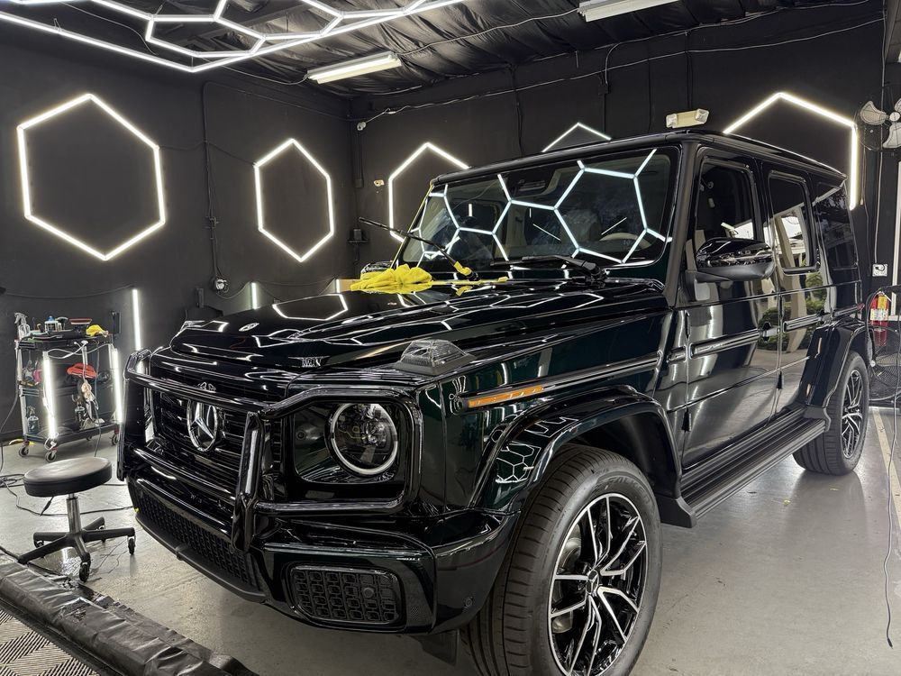Black Mercedes G-Class SUV in a modern showroom with hexagonal lights and a yellow ribbon on the hood