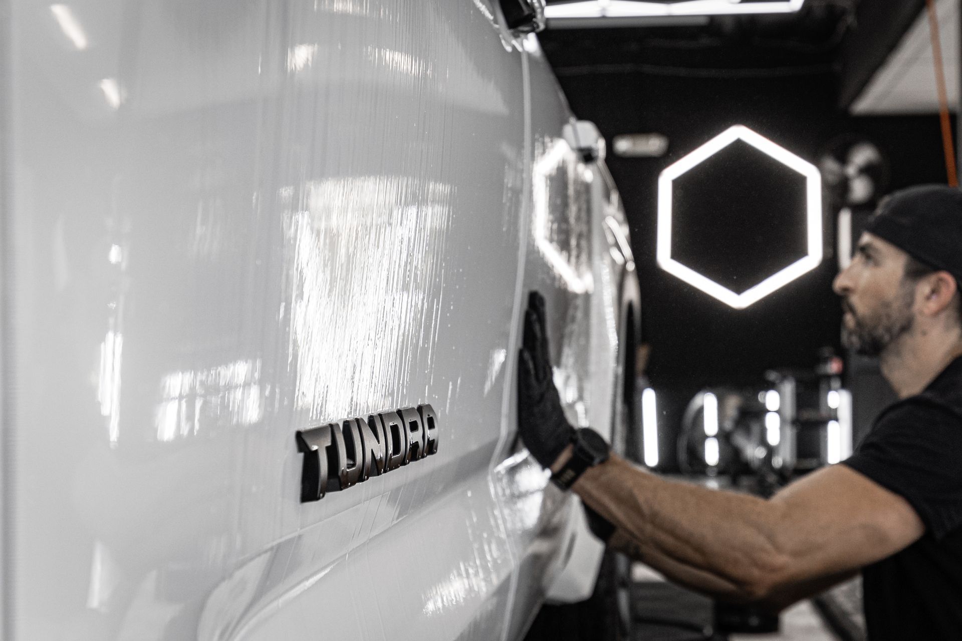 Man polishing a white Toyota Tundra in a glossy auto detail shop