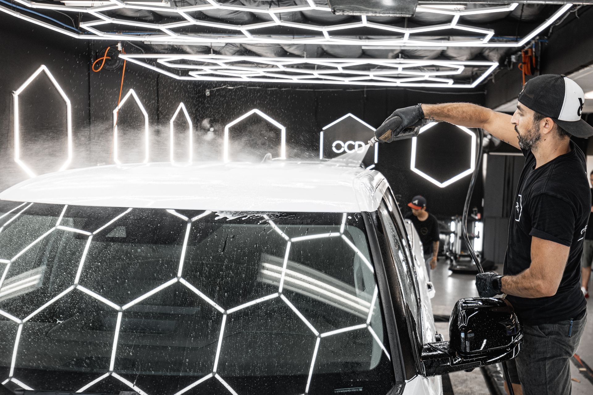 Man applying glowing hexagonal vinyl wrap to a car in a workshop