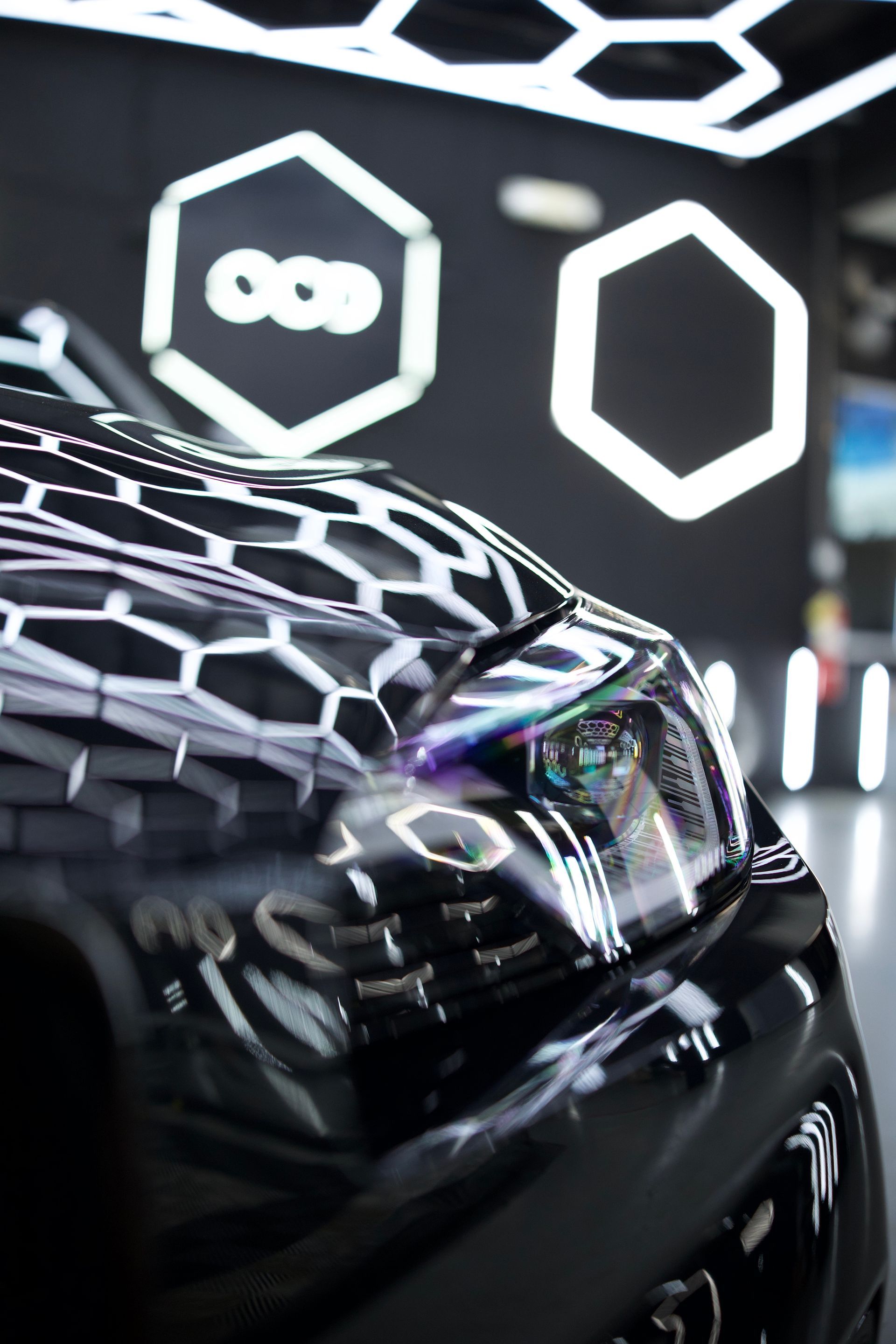Close-up of a glossy black car front under bright hexagonal showroom lights