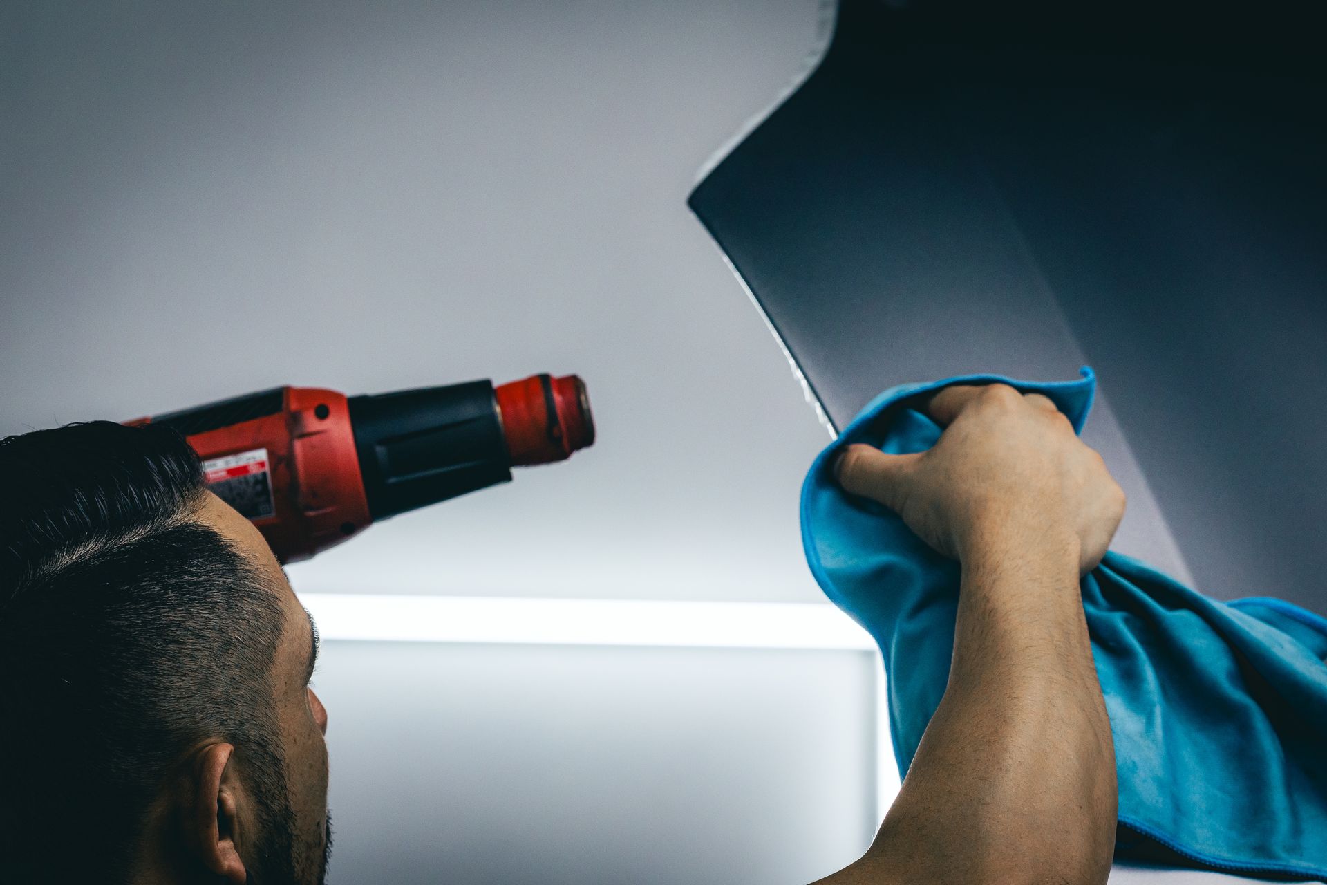 Person using a red power drill while holding blue fabric against a white ceiling panel