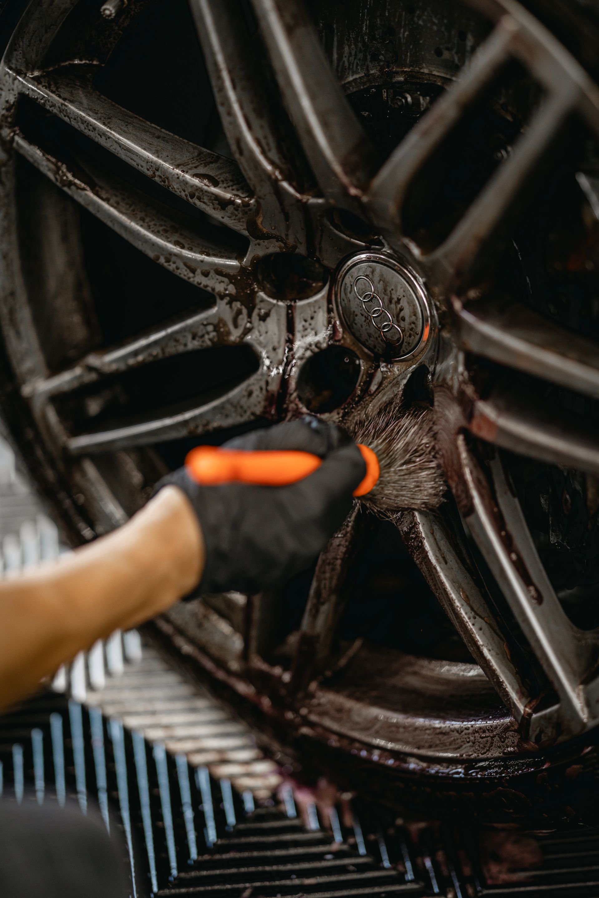Gloved hand cleaning a muddy car wheel with a brush