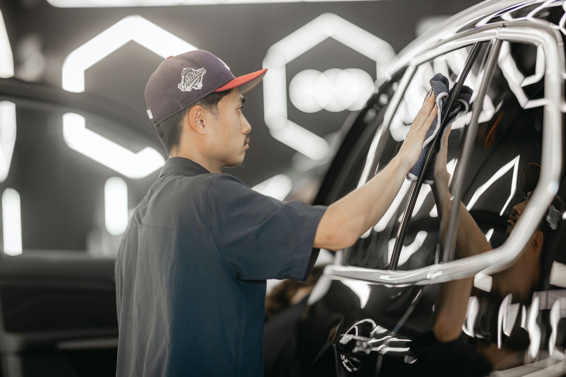 Person wiping a black car in a garage with bright geometric lights in the background