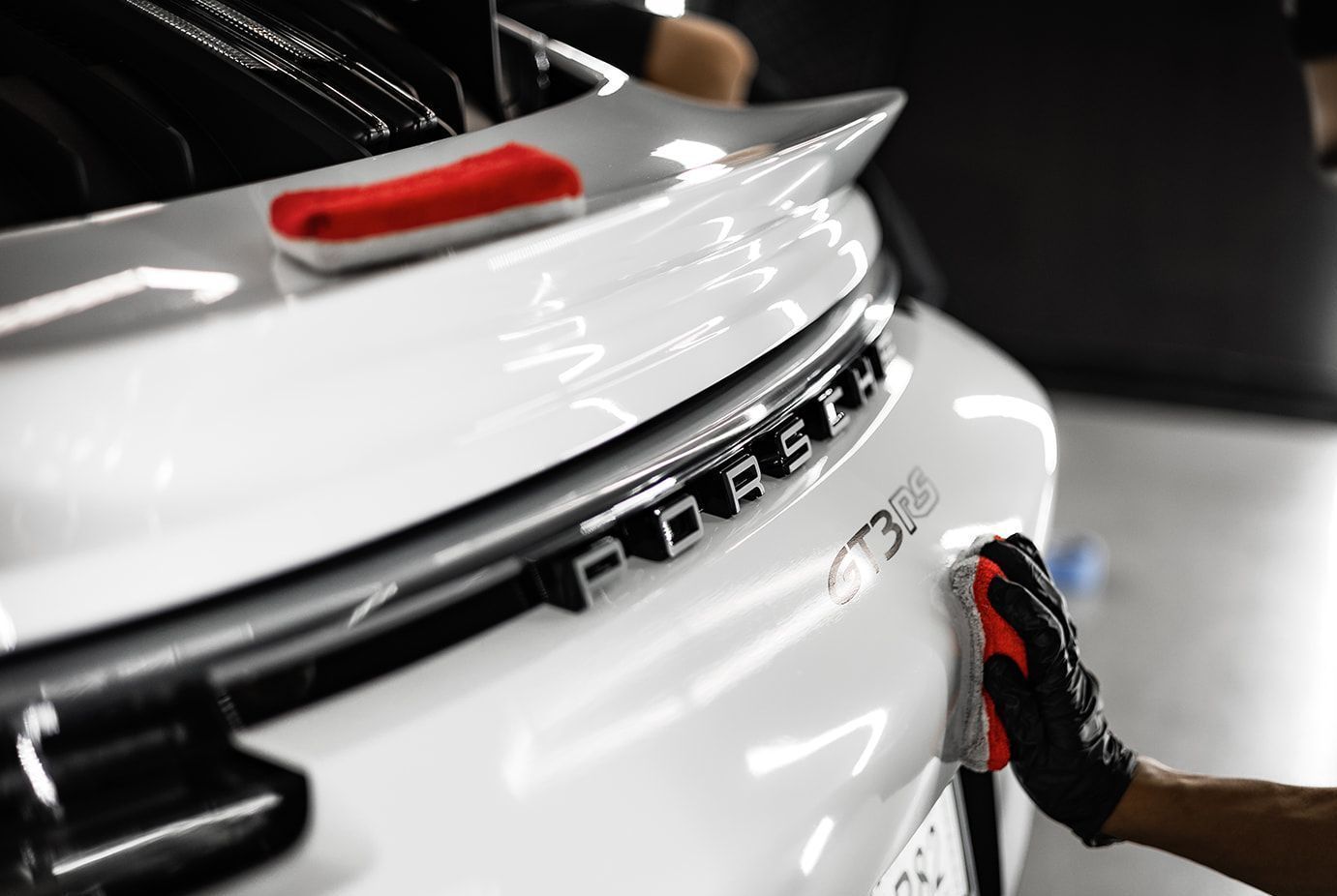 A hand wipes the rear of a white Porsche with a red cloth.