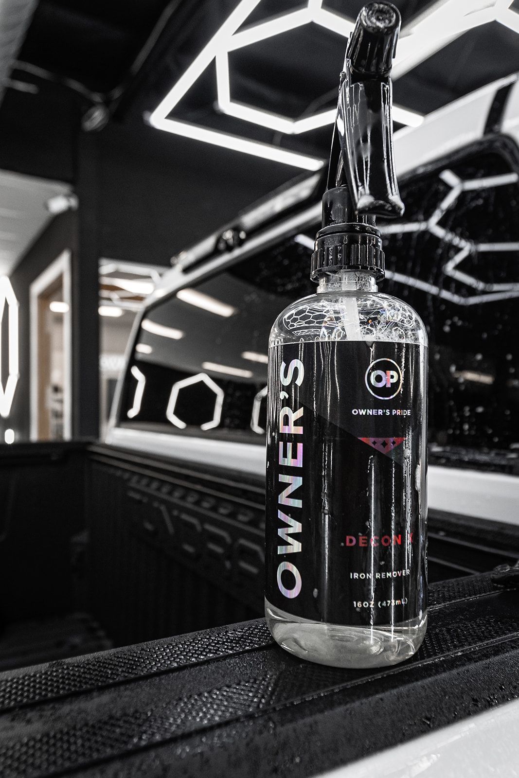 Black OWNER'S PRIDE bottle on a reflective surface in a modern black-and-white showroom
