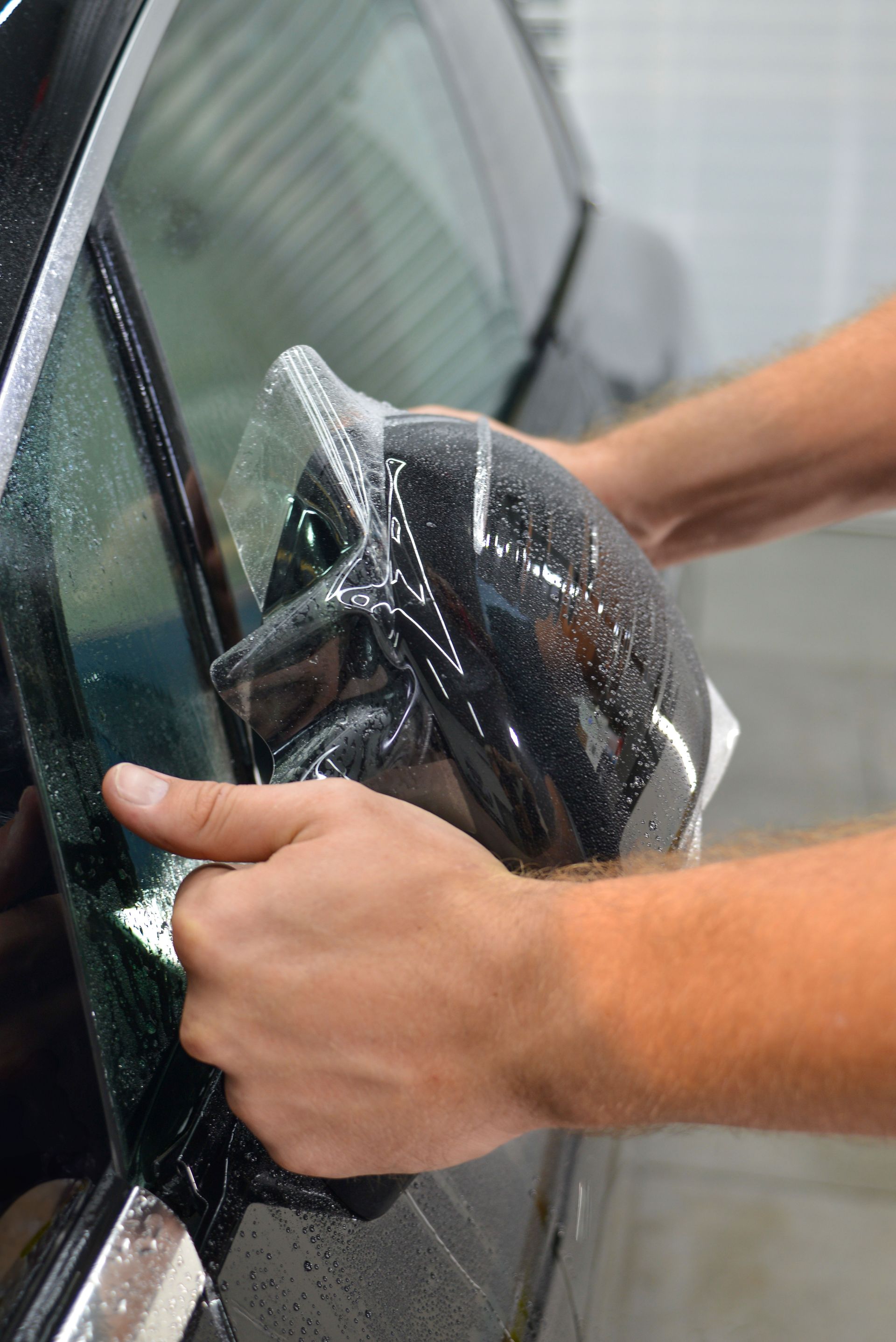 Hands applying protective film to a car side mirror outdoors