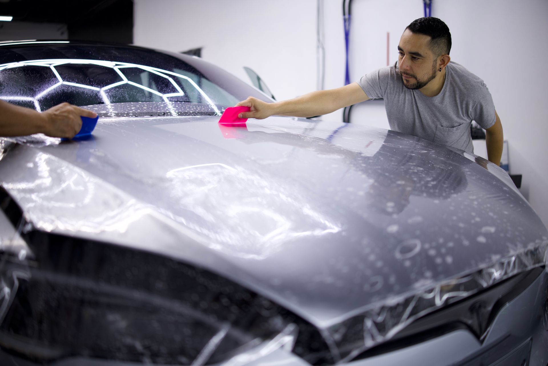 Two people applying ppf to car hood