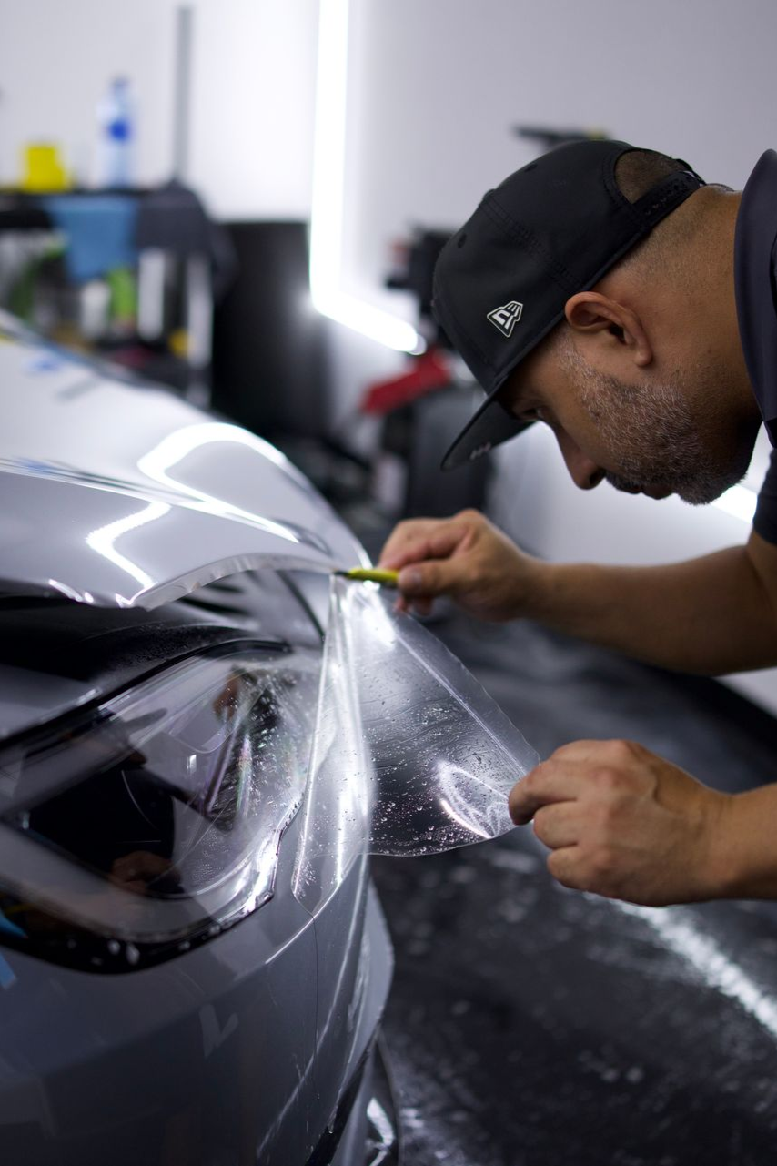 Man wrapping clear protective film on a gray car hood in a workshop