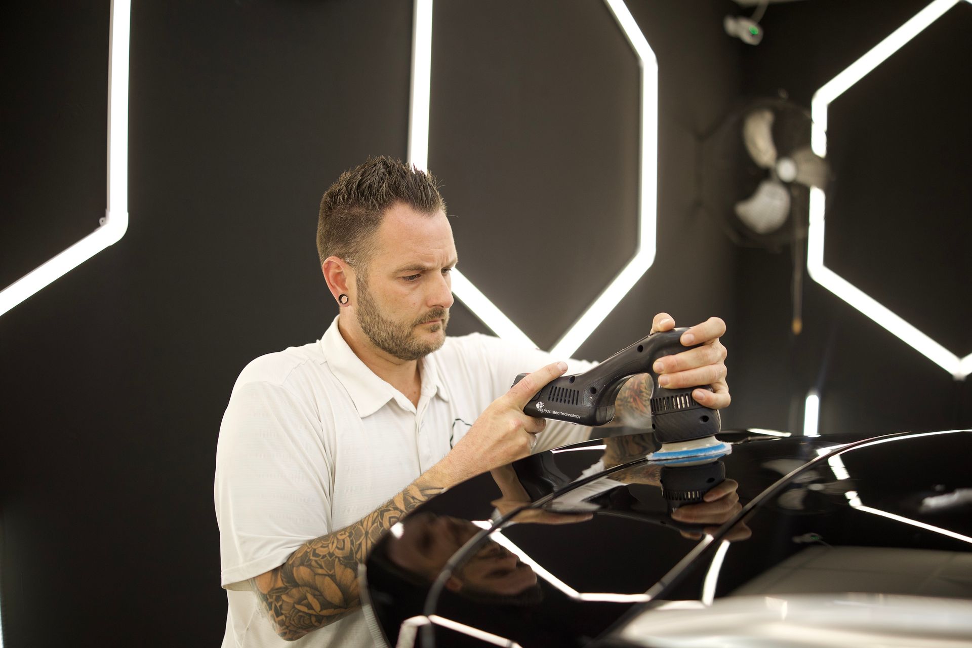 Technician applying protective film to a black car in a workshop with bright geometric lights