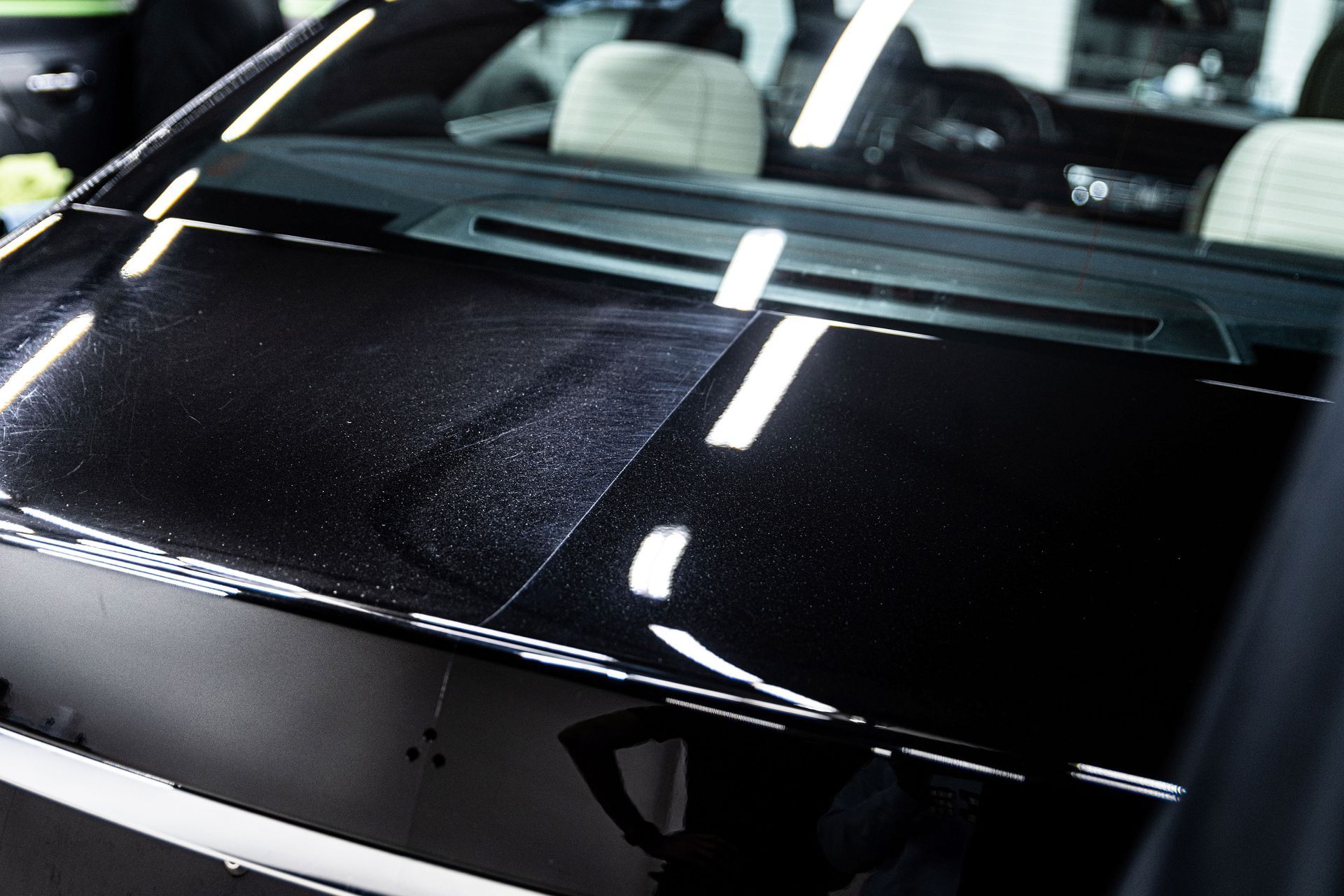 Close-up of a glossy black car hood with bright light reflections in a showroom-like setting