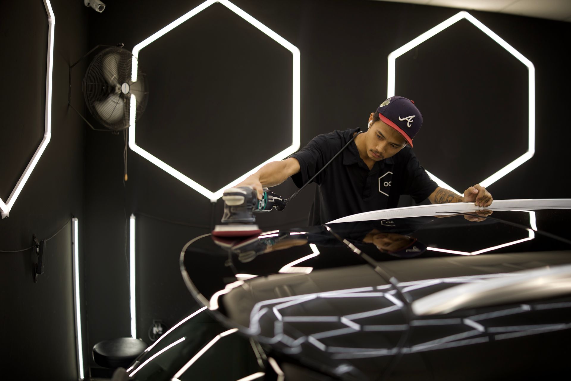Person polishing a black sports car in a studio with glowing hexagonal wall lights