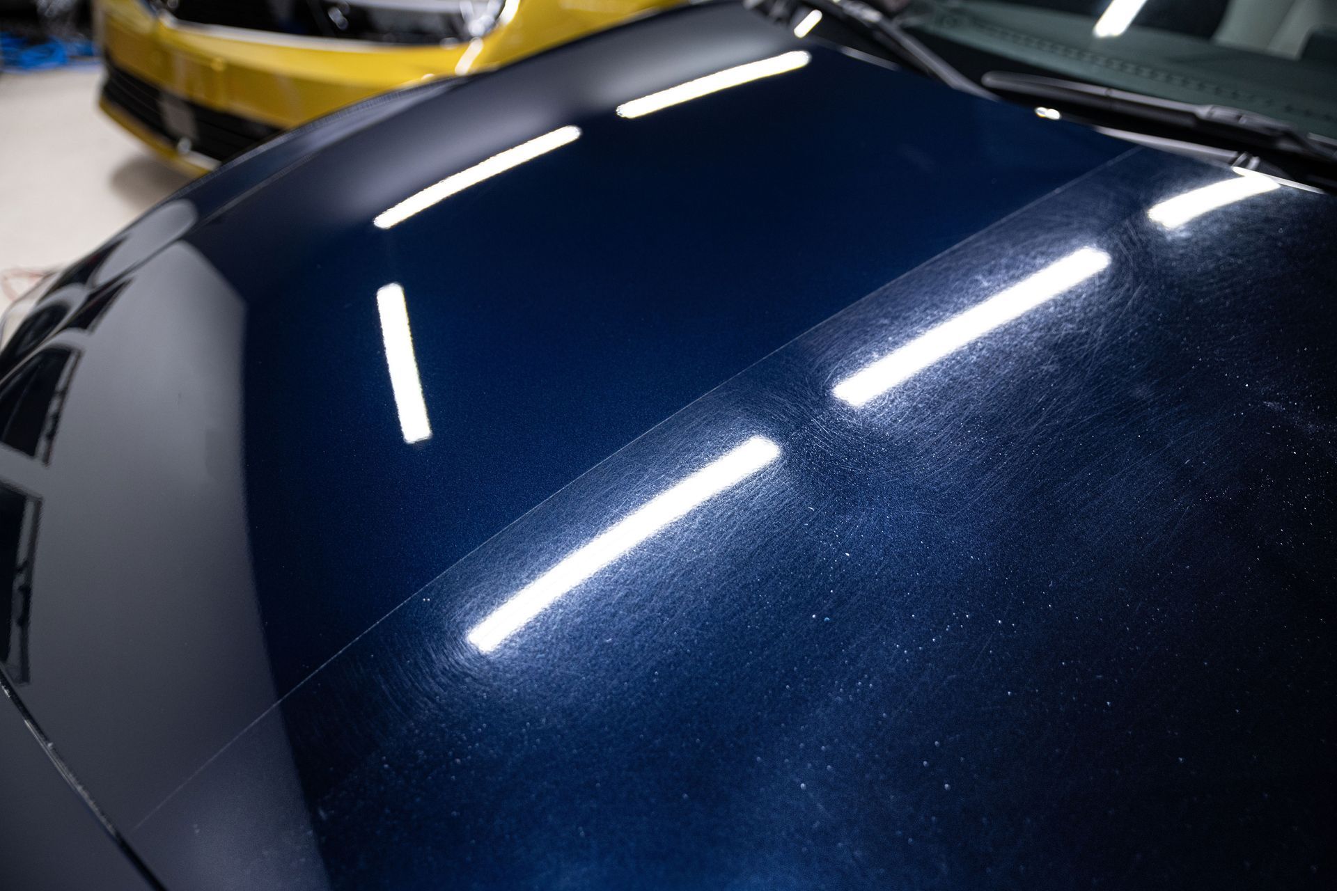 Close-up of a dark blue car hood with bright white reflections under indoor lights