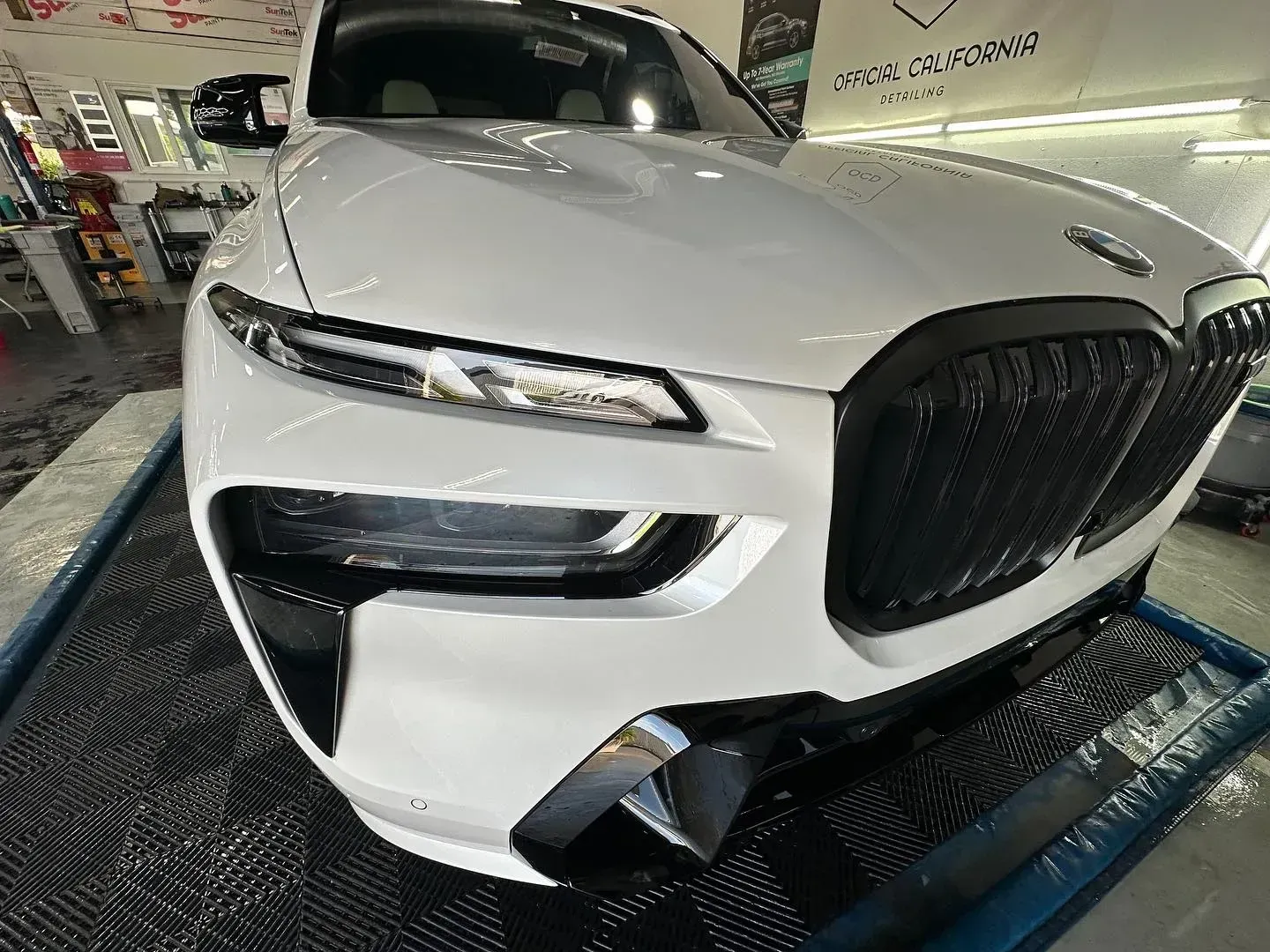 White BMW sedan parked indoors on a car lift, front view with large black grille and headlights on display