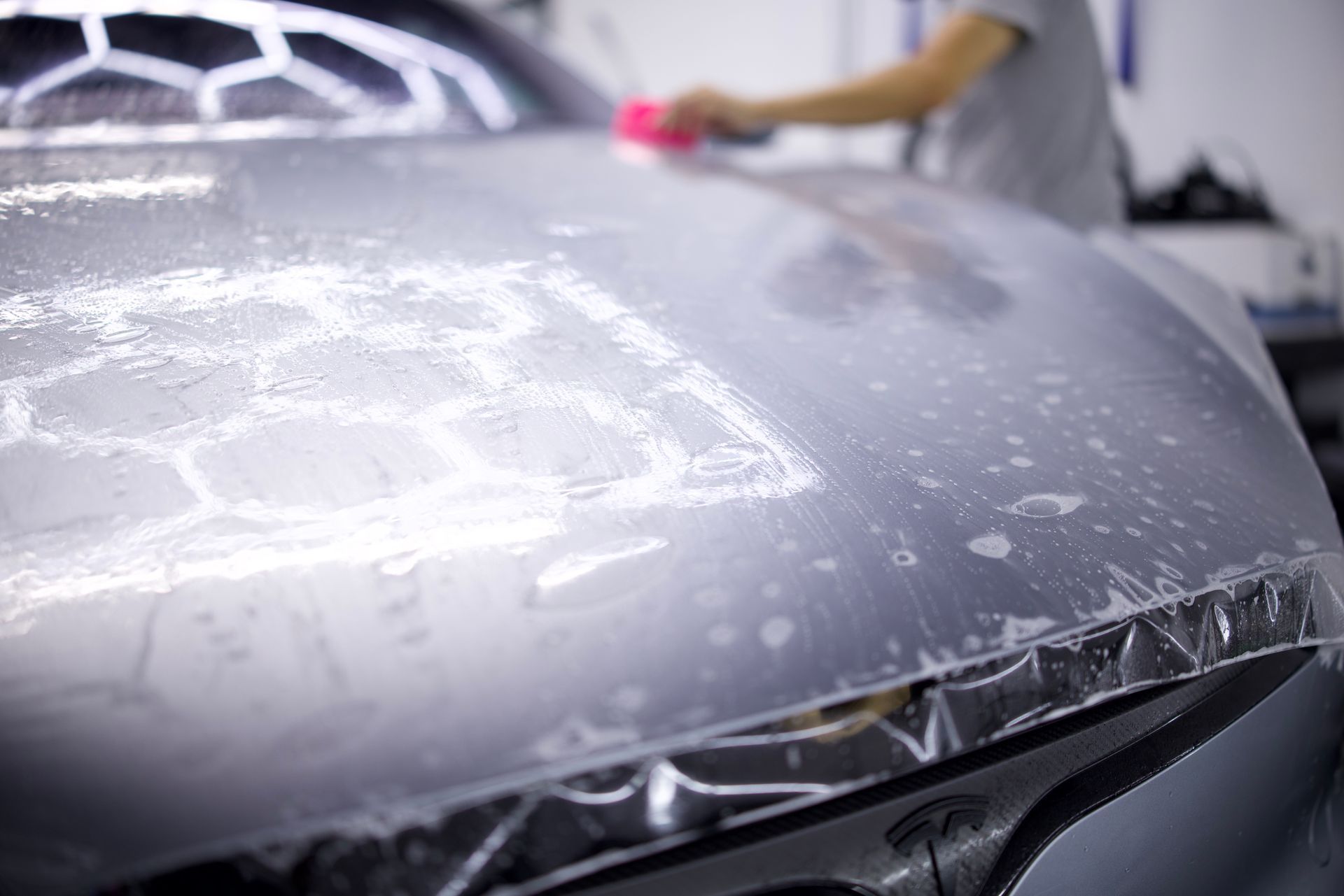 Close-up of a gray car hood being polished with soap foam in a workshop