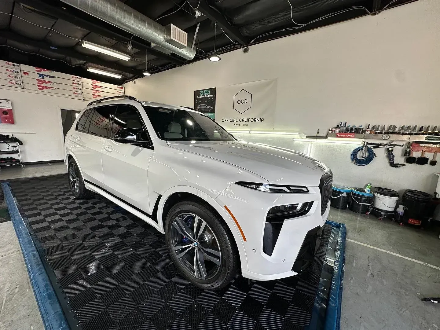 White SUV in a showroom or workshop, parked on a dark patterned floor with tools on the wall behind it