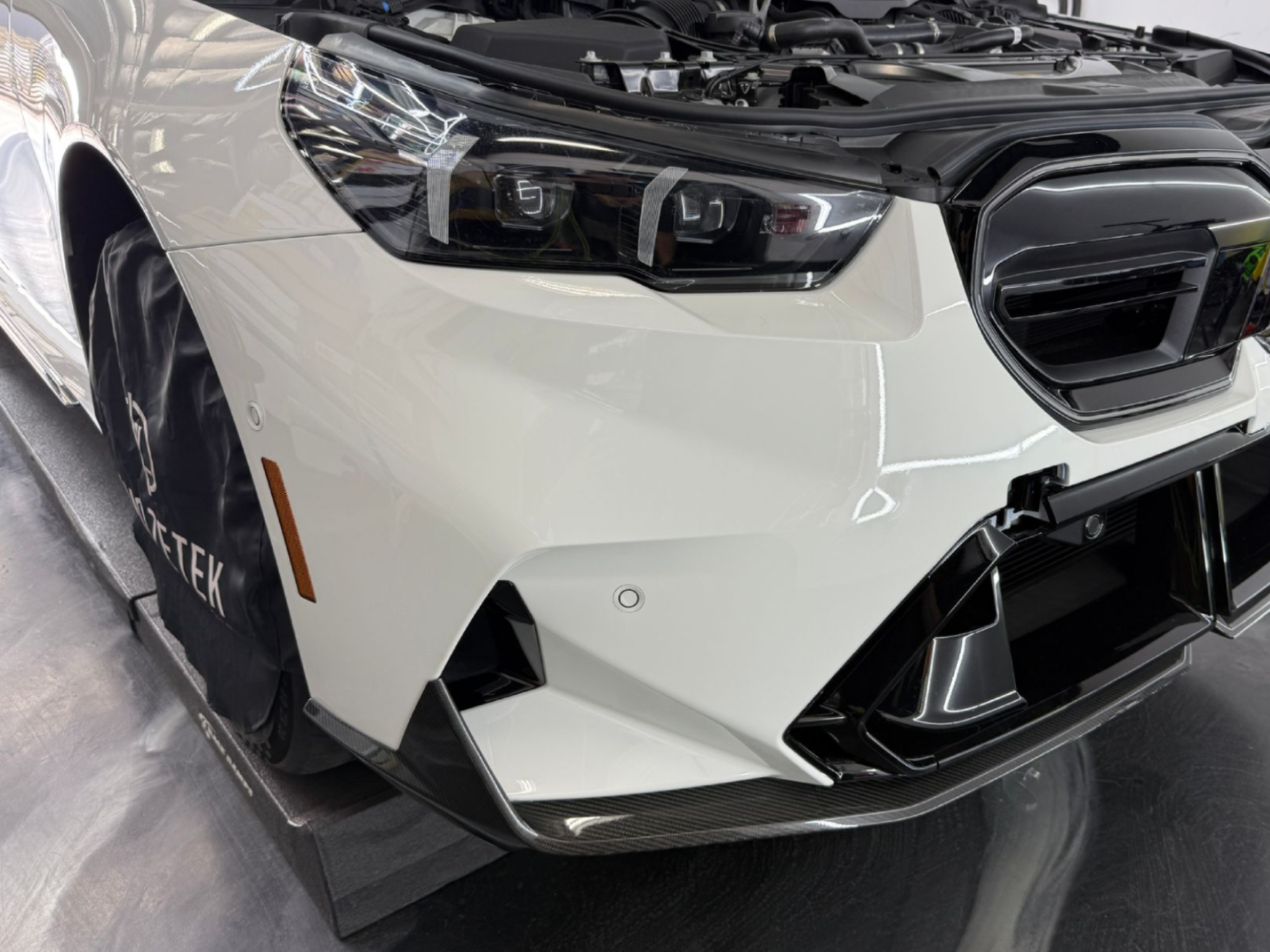 White BMW sedan with front-end damage in a garage, showing a cracked bumper and headlight area