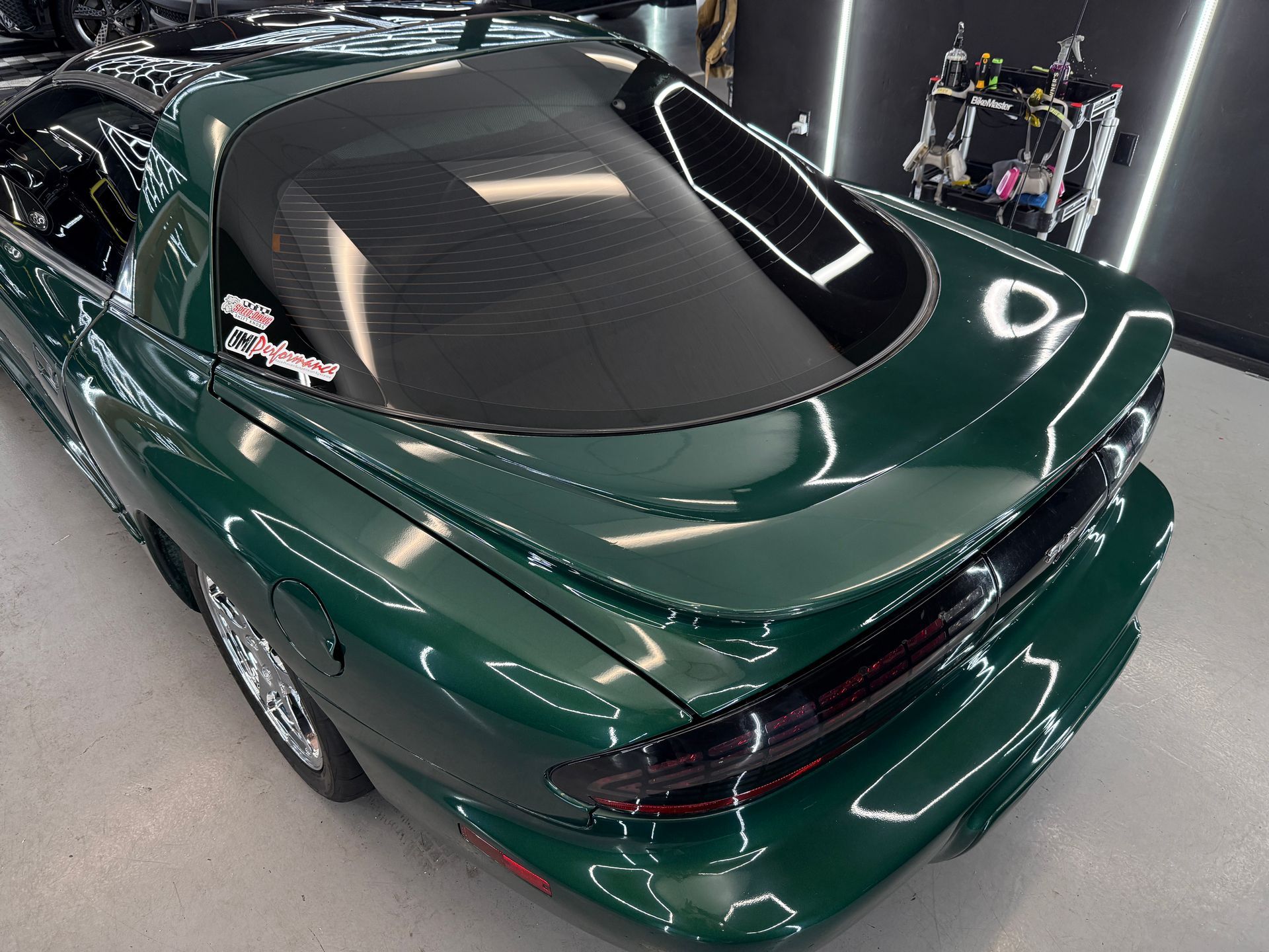 Dark green sports coupe in a garage, shown from the rear with a glossy black roof and spoiler.