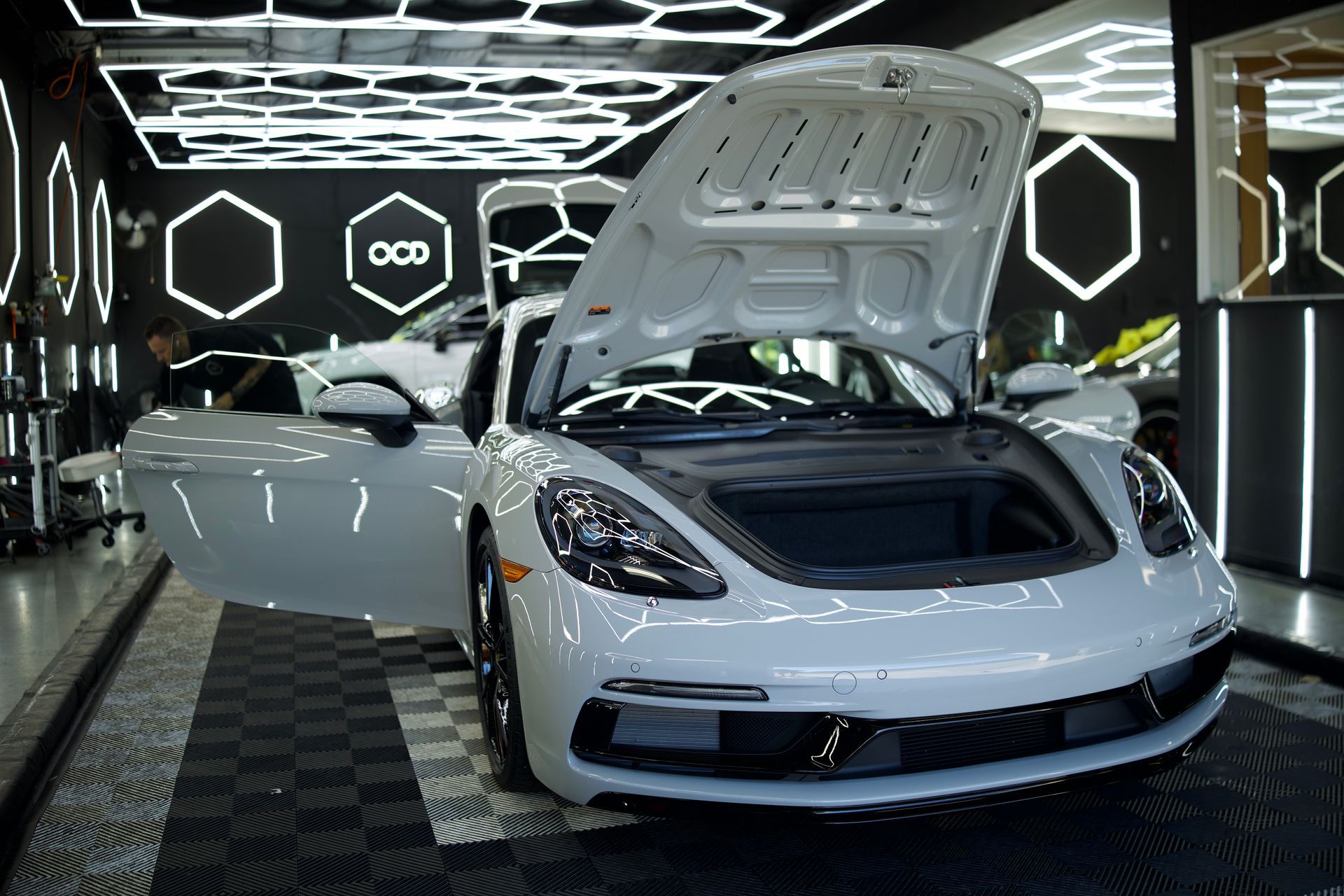 White sports car with open hood and doors in a futuristic showroom with neon hexagon lights