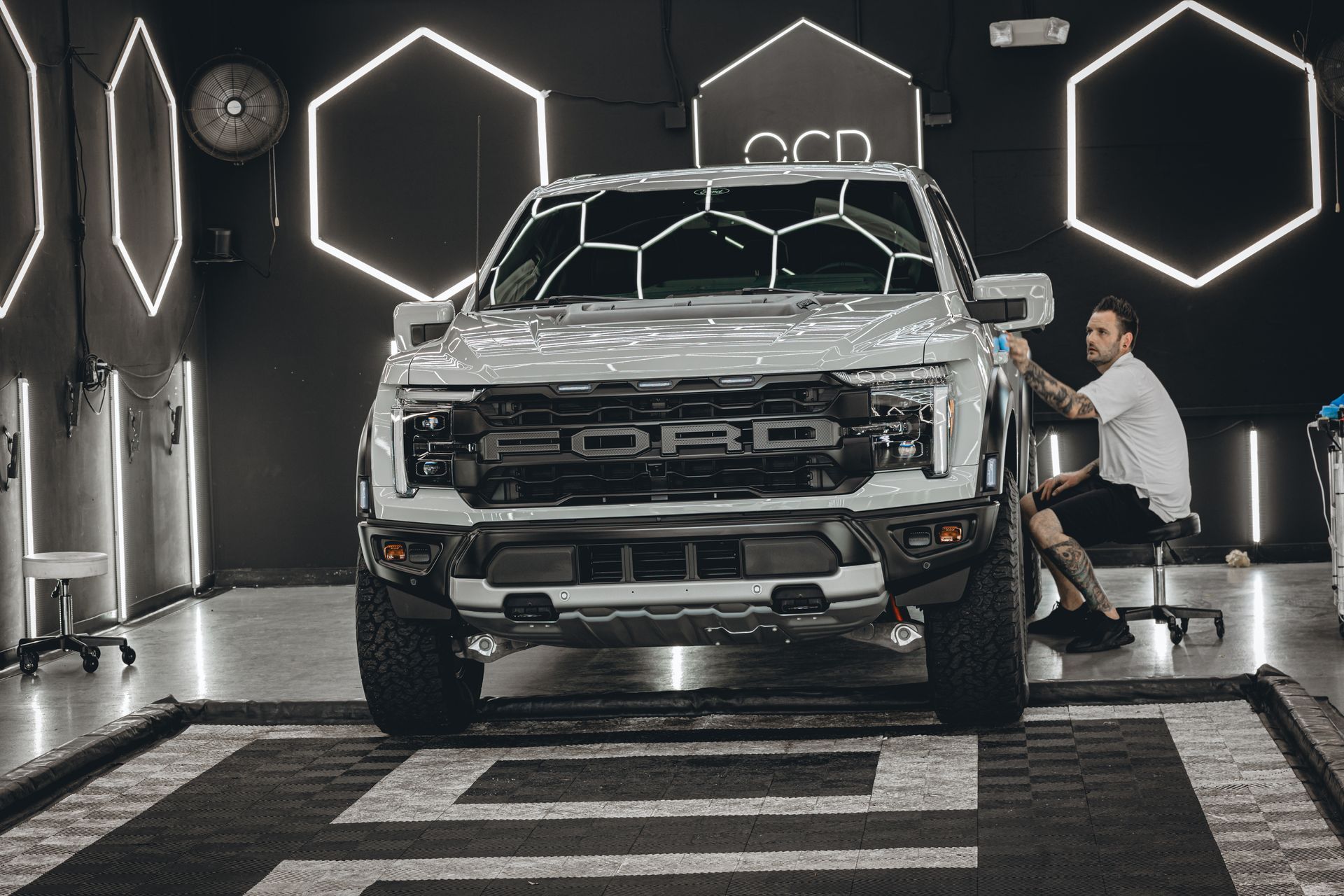 Man polishing the front of a silver pickup truck in a modern detailing garage with hexagonal lights