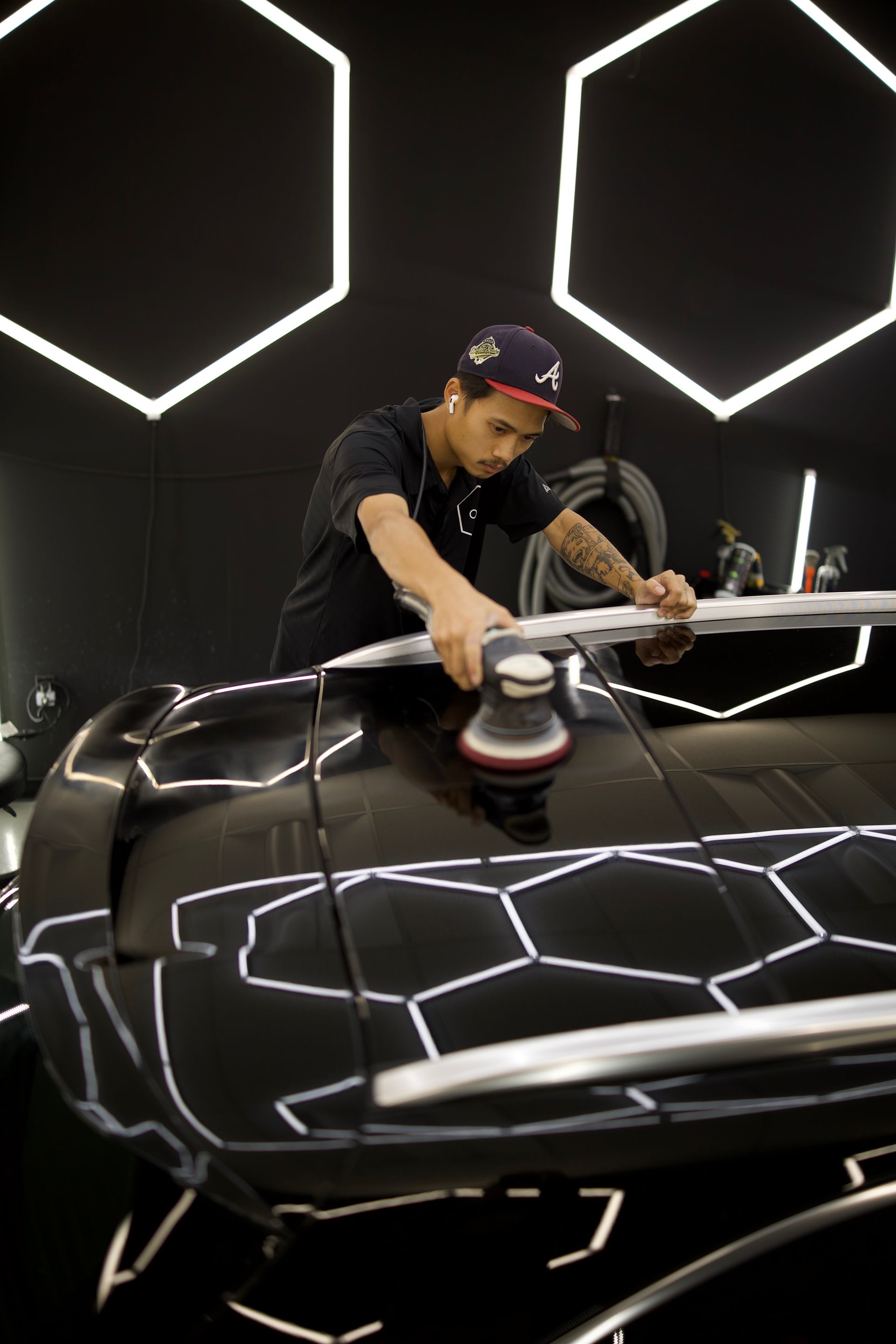 Person polishing a black car in a studio with bright hexagonal lights overhead