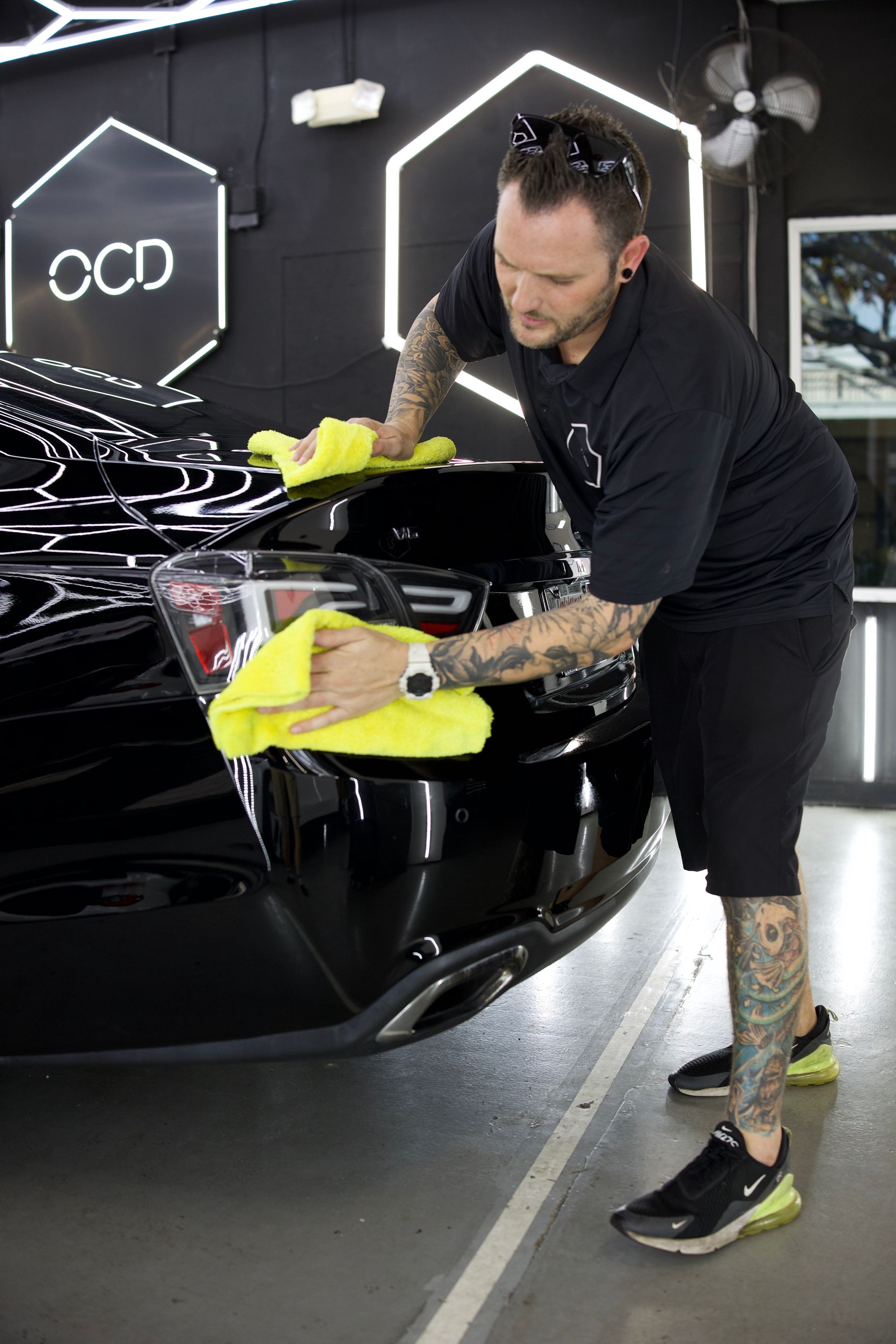 Detailing a black car’s hood with a yellow cloth in a car wash garage