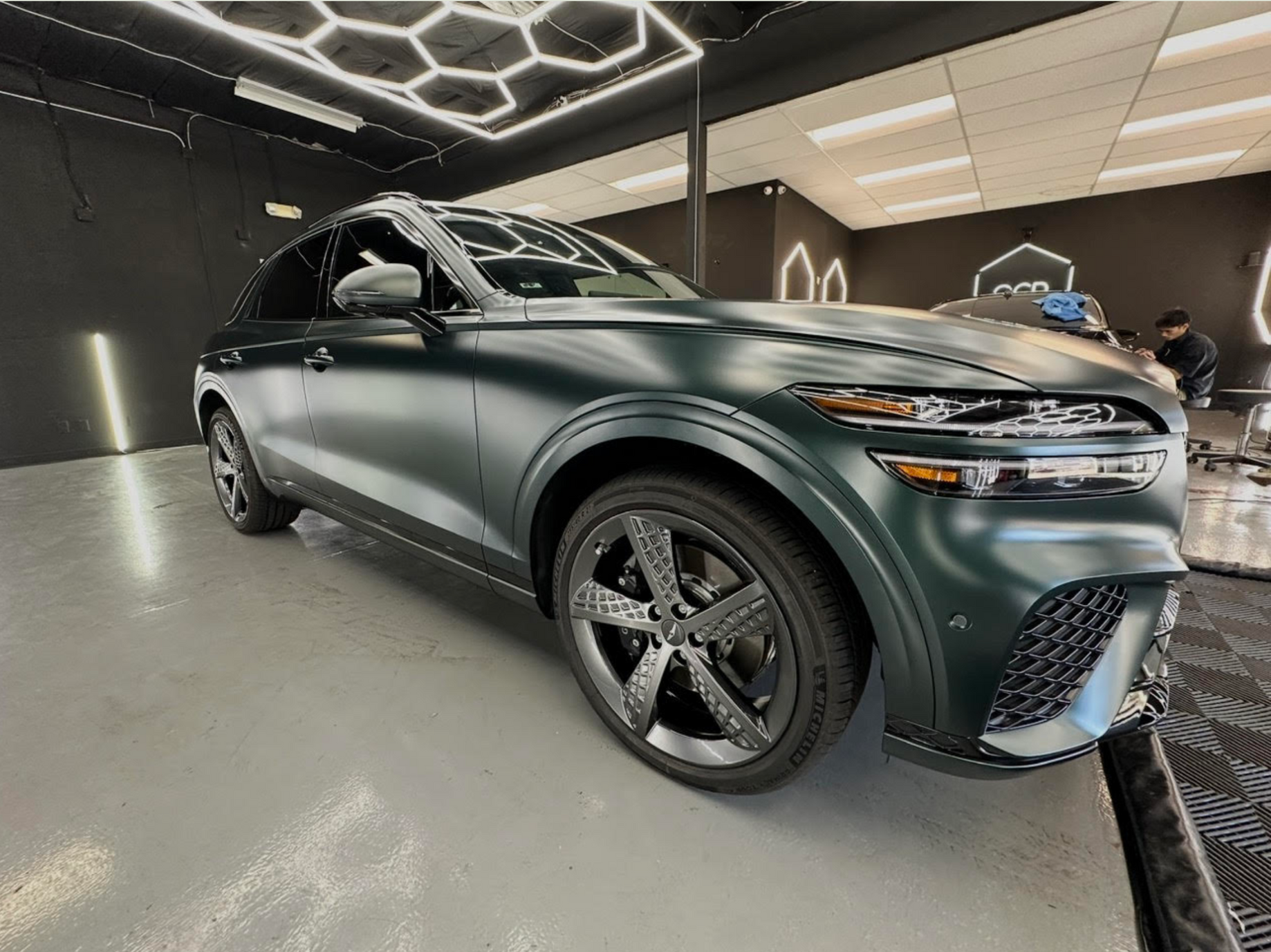 Dark green SUV in a showroom with geometric ceiling lights and glossy black wheels