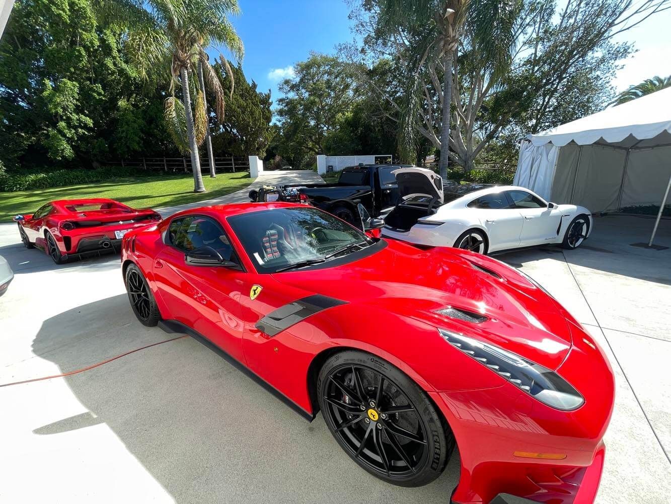 Red sports cars parked outdoors at a sunny car show, with a white tent and trees nearby