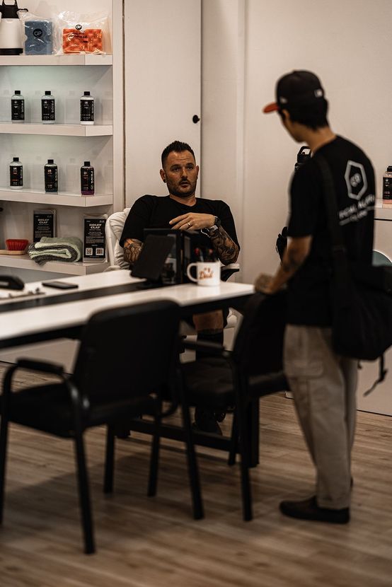 Two people talk in a modern office break room beside a counter and shelves.