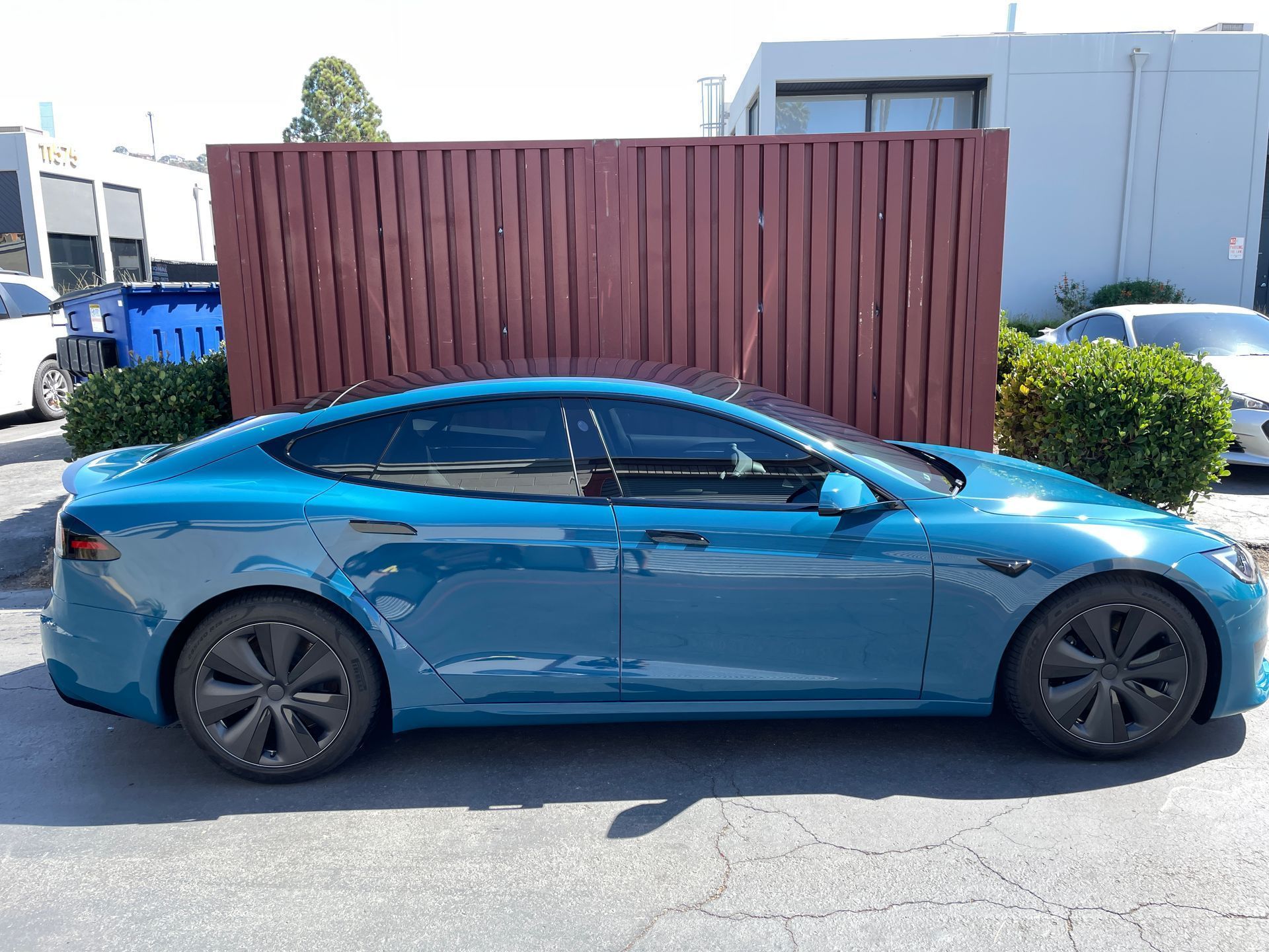 Blue sedan parked beside a brown wooden fence in a sunny lot