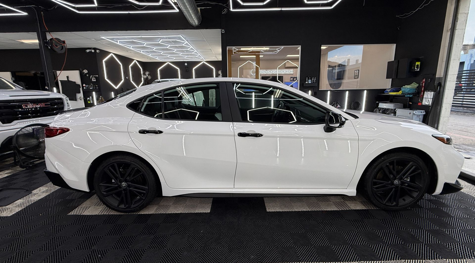 White sedan in a showroom with geometric ceiling lights and black patterned floor.
