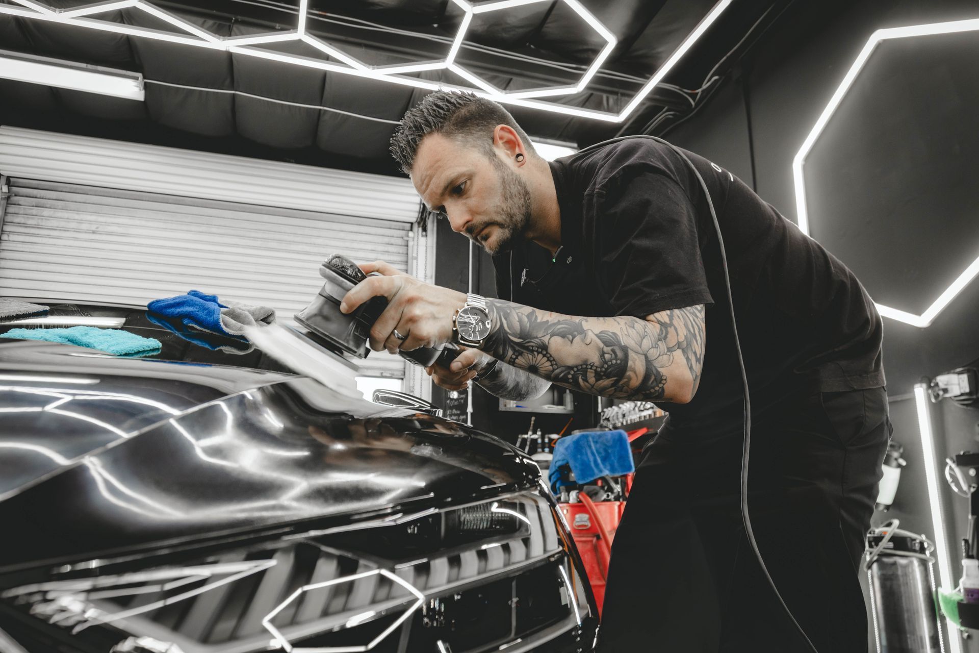 Detailer polishing a black car in a neon-lit garage