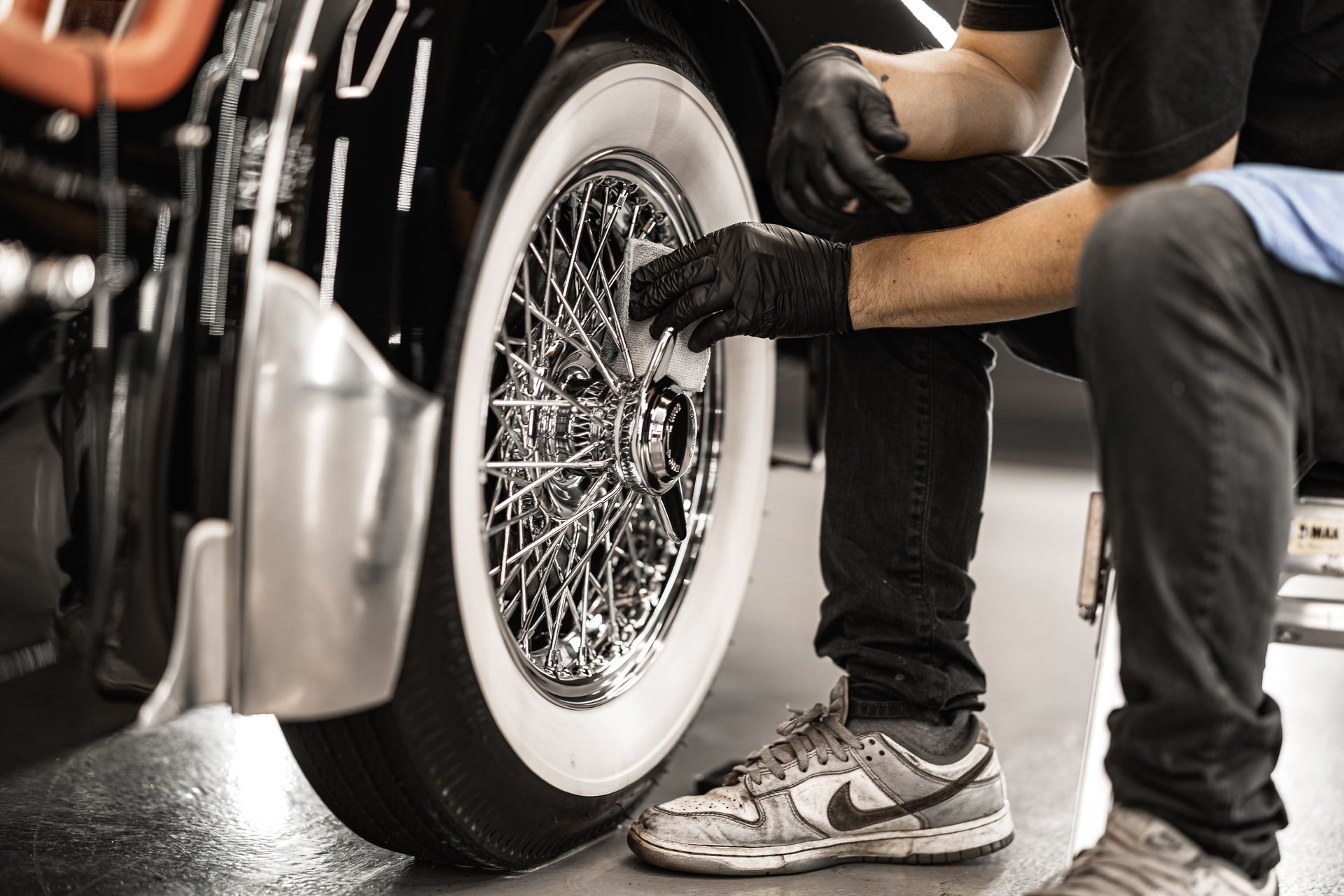 Mechanic working on a car’s whitewall tire and wire wheel in a garage