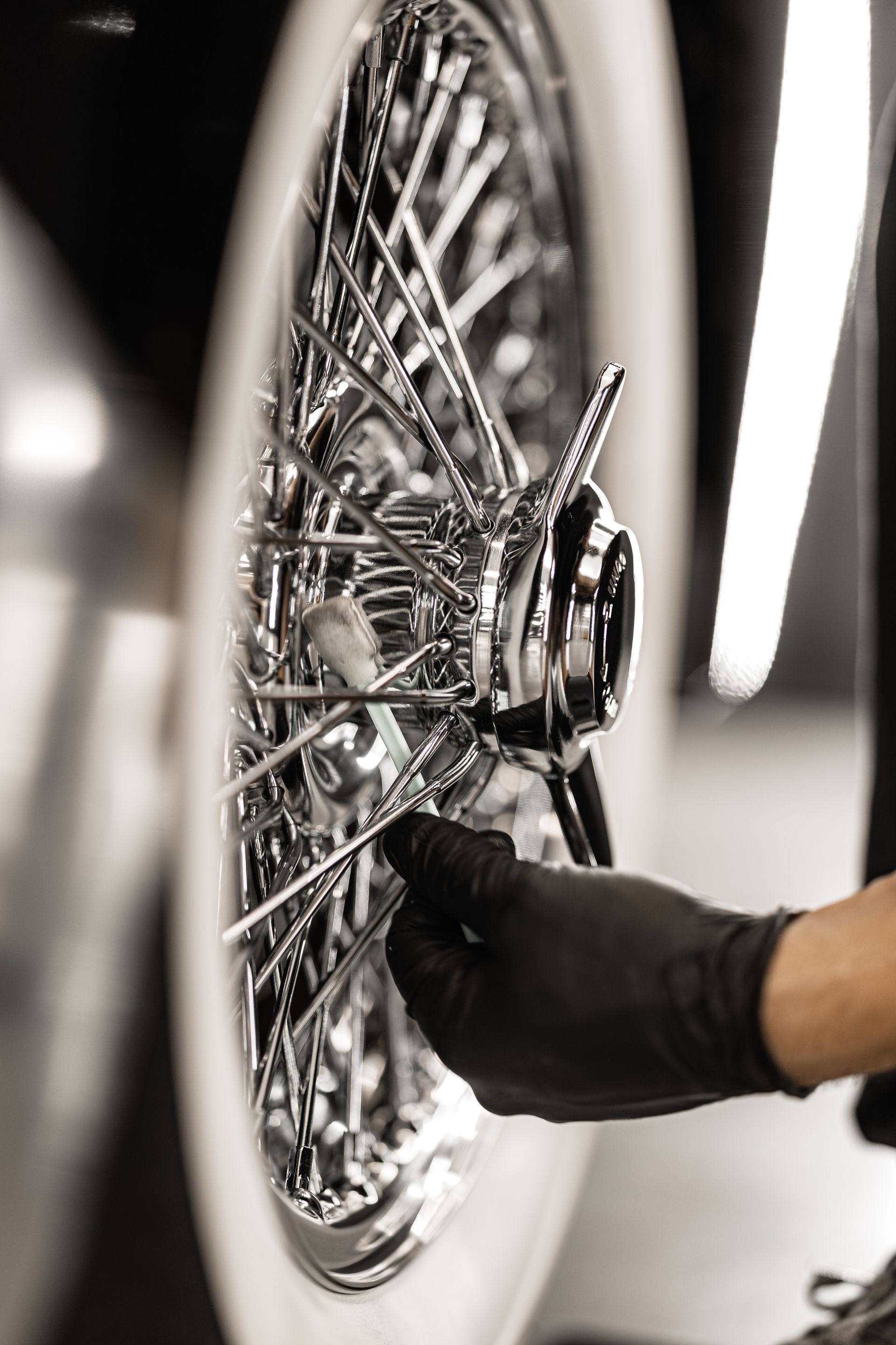 Black-gloved hand polishing a chrome wire wheel on a car in a garage