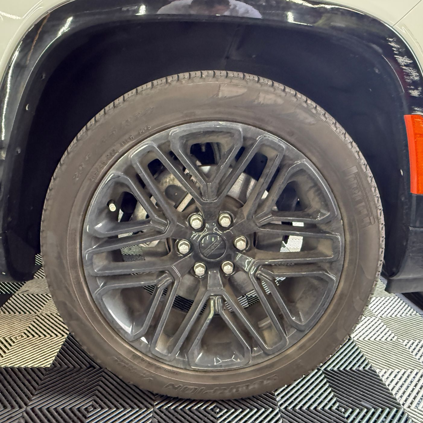Close-up of a black car wheel and tire on a checkered showroom floor.