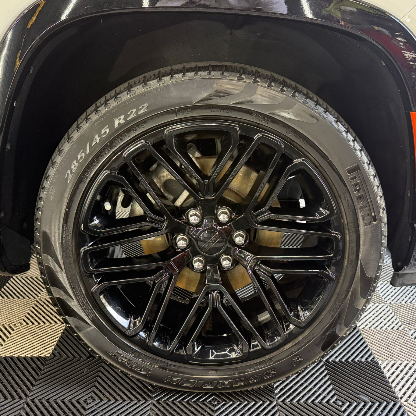 Close-up of a black and silver car wheel on a red vehicle, shown on a checkered floor.