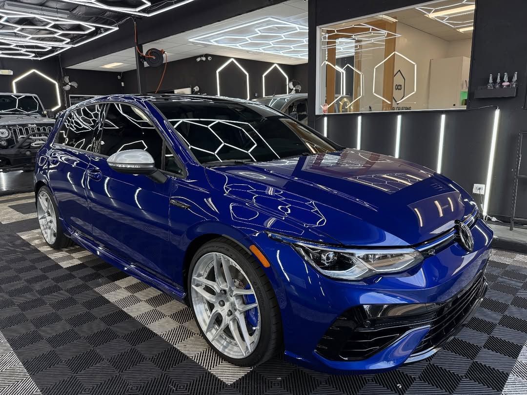 Blue sports sedan in a showroom with geometric wall lights and patterned black floor.