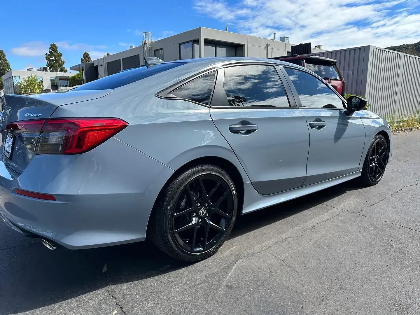 Silver sedan parked on a sunny street beside a warehouse, shown from the rear side.
