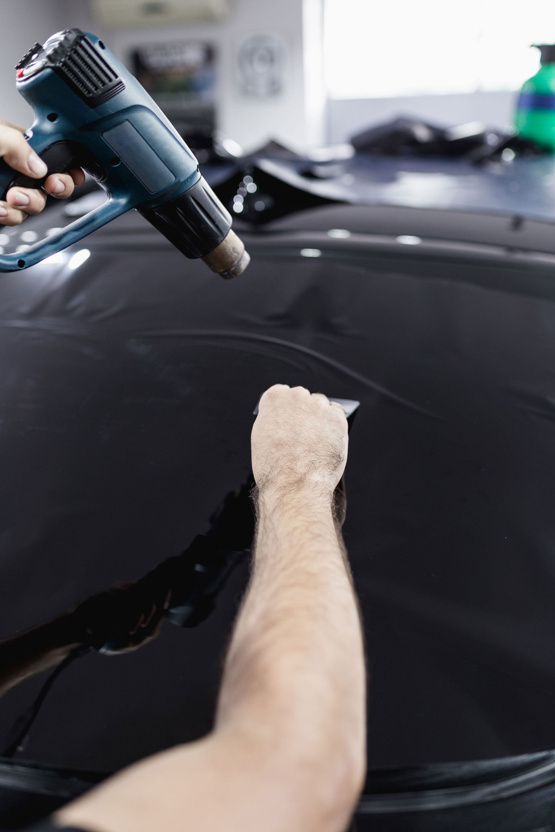 Person using a heat gun on a glossy black car surface during detailing