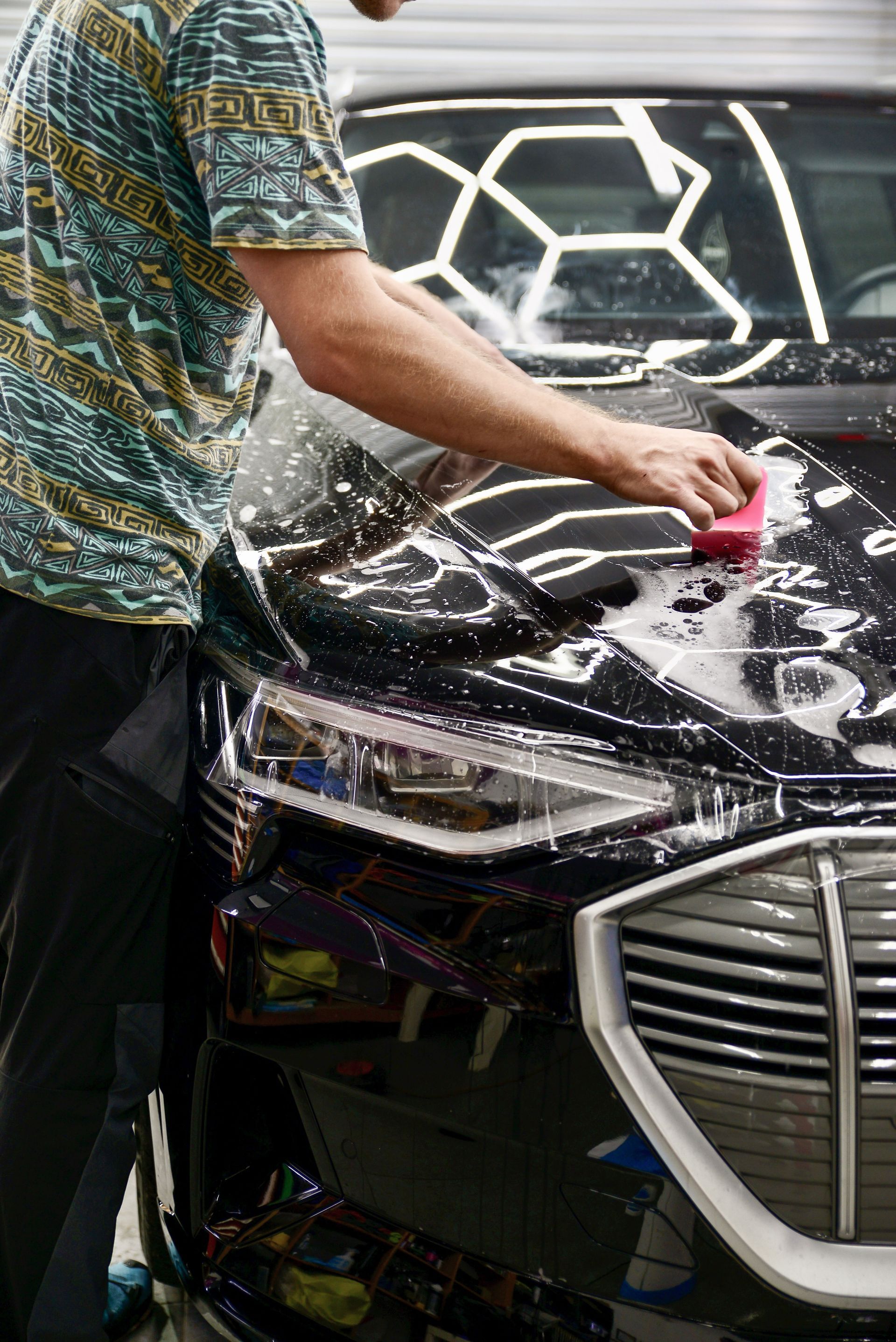 Person washing the front of a black car with a pink sponge outdoors