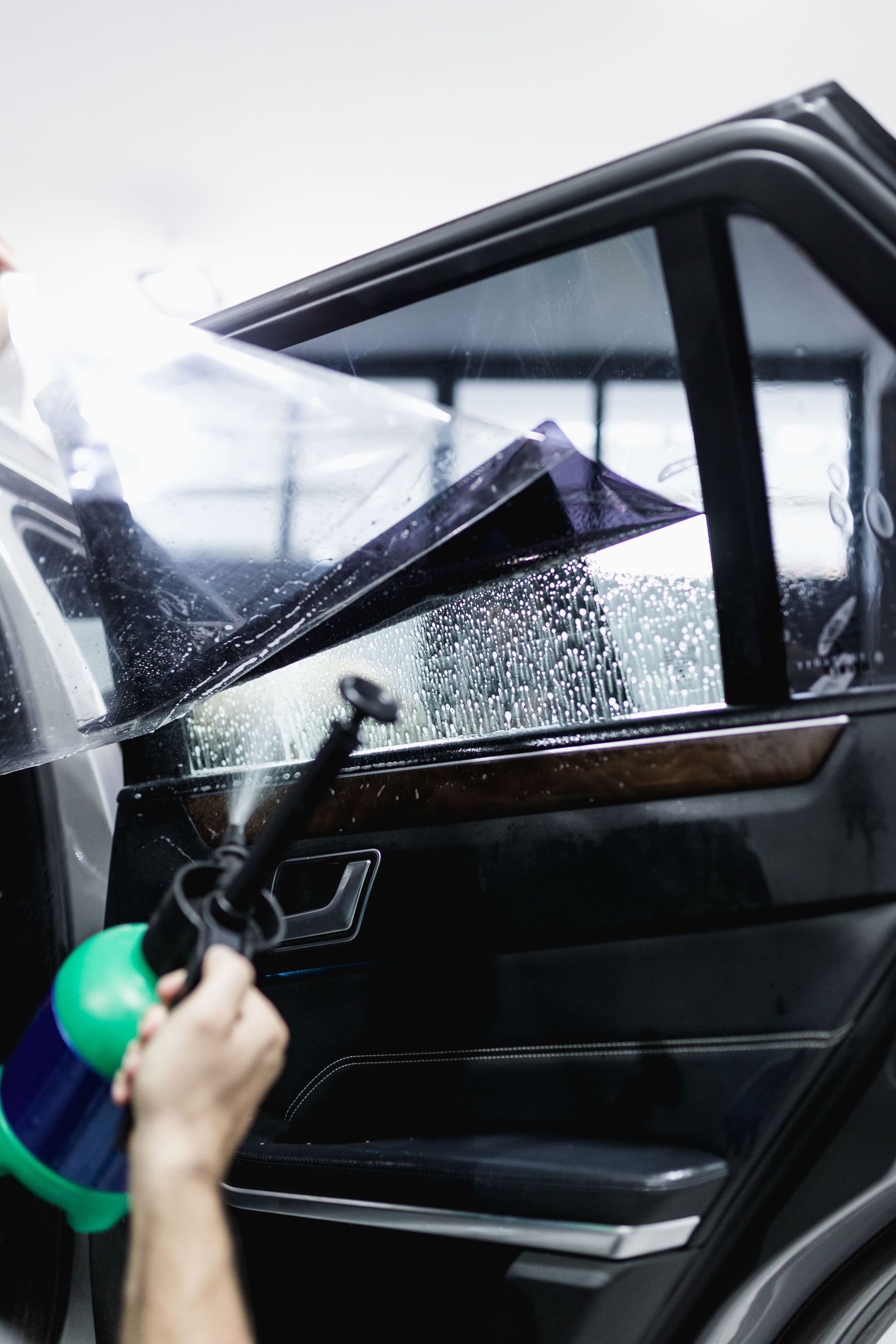 Person washing a black car hood with a sponge in a car wash area