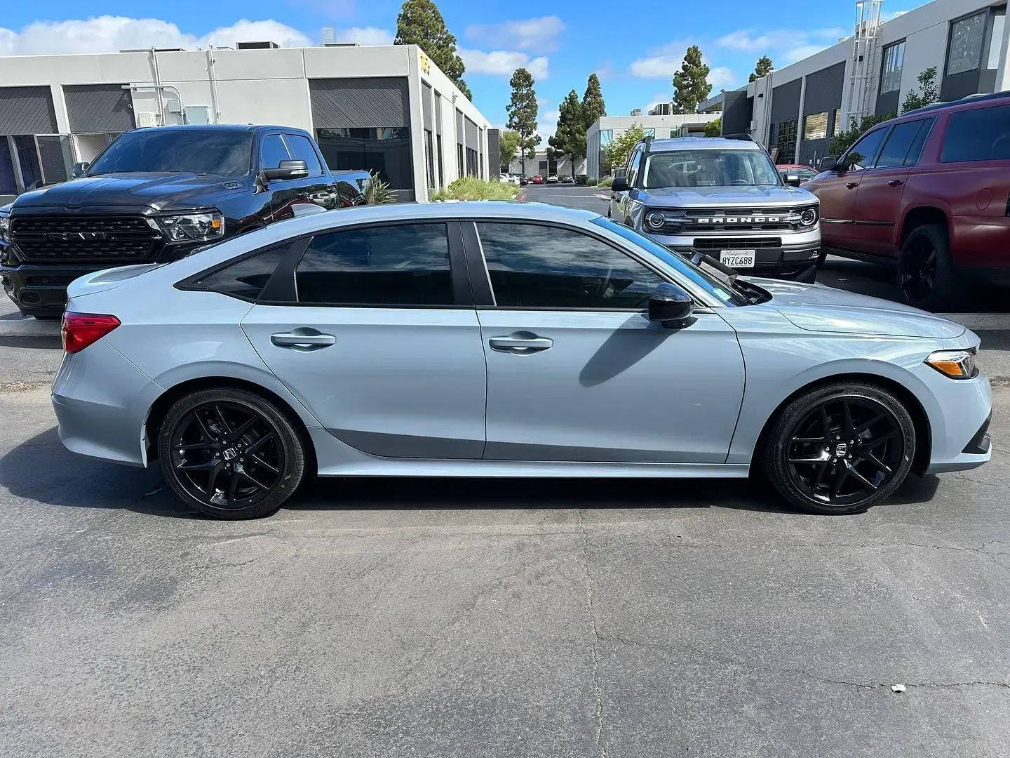 Silver sedan parked in a lot, side view, with black rims and trucks in the background